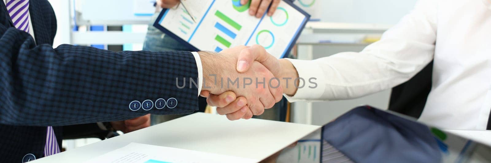 Handshake of business people at meeting and signing agreement. Working group of team at conference discusses financial chart and concludes business contract