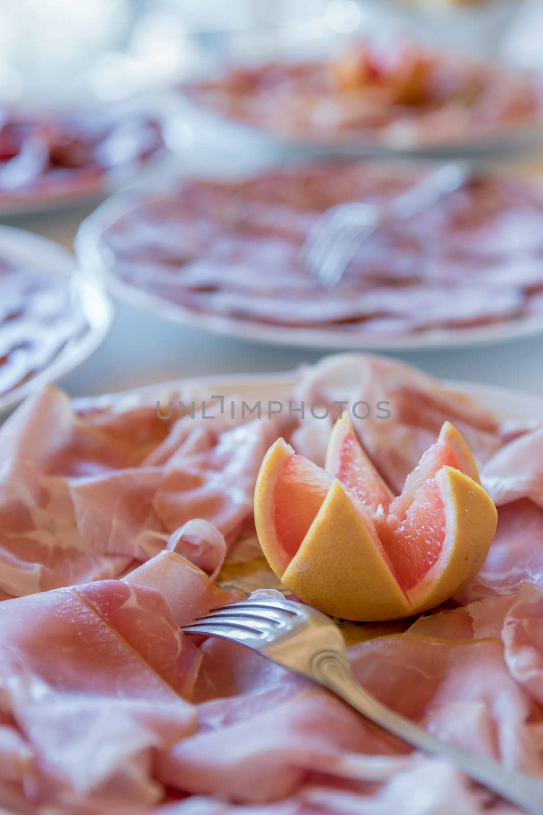 Plate of cooked ham with orange as decoration. Party, holiday. Defocused background.