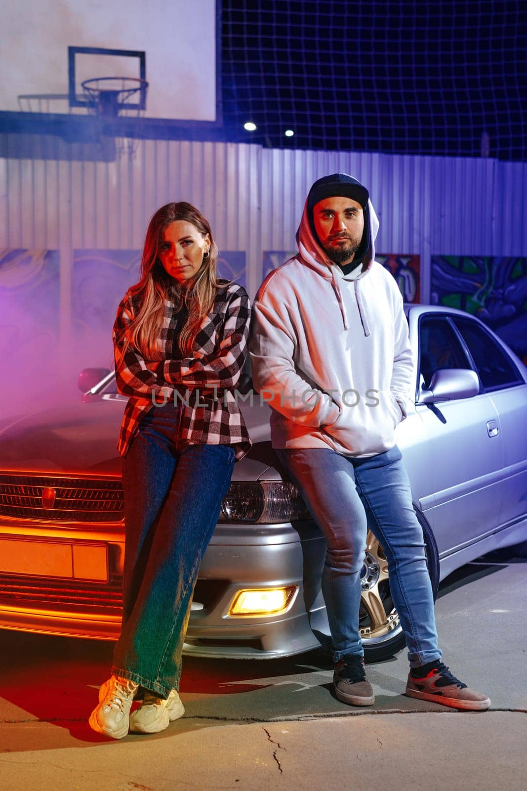 Smiling loving couple standing near sport car over night city background