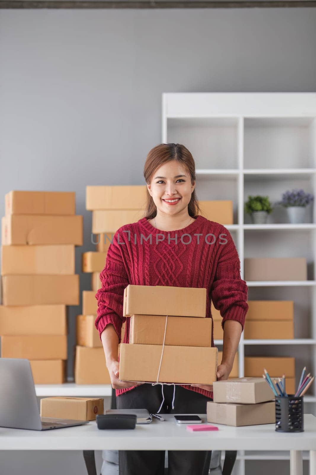 Starting small business entrepreneur of independent Asian woman smiling using computer laptop with cheerful success of online marketing package box items and SME delivery concept by wichayada