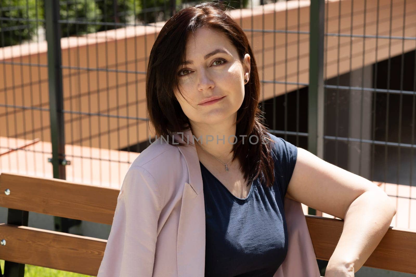 Portrait Beautiful Brunette Mature Woman Sitting On A Bench In Residential Campus. Female Is Dressed In Casual Clothes. Rest And Relaxation. Horizontal Plane. High quality photo