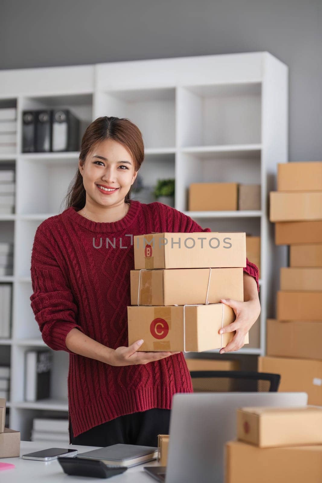 Starting small business entrepreneur of independent Asian woman smiling using computer laptop with cheerful success of online marketing package box items and SME delivery concept by wichayada