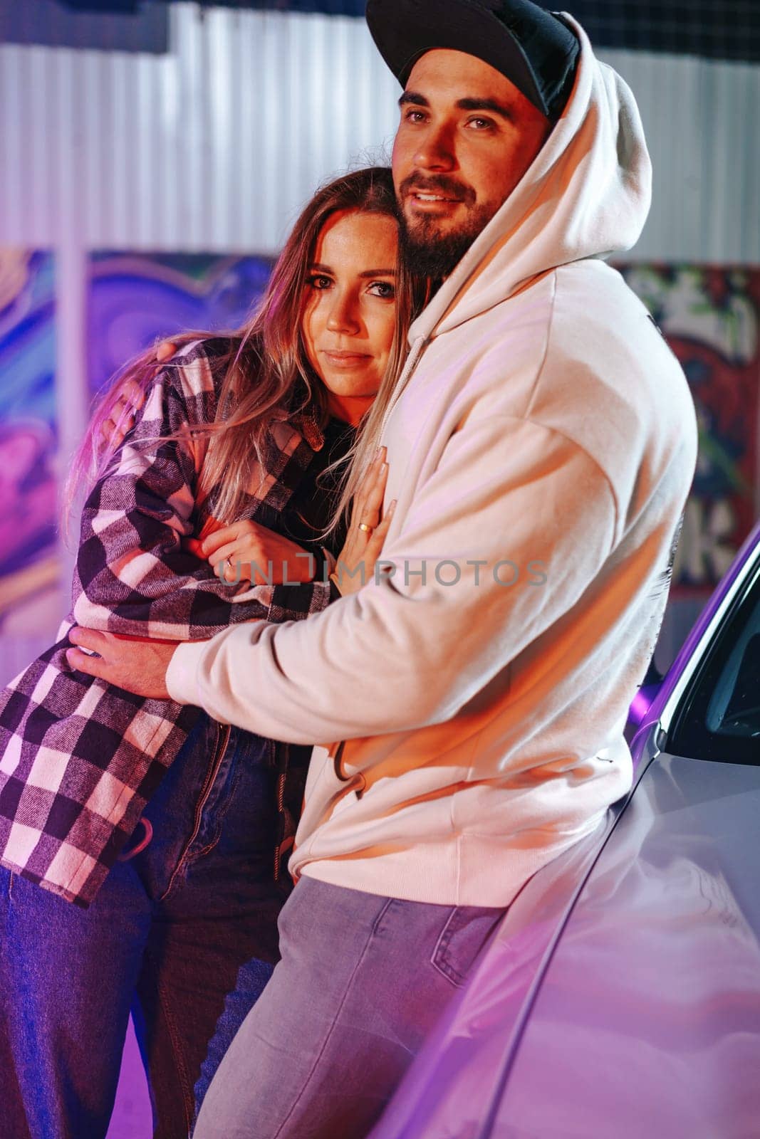 Smiling loving couple standing near sport car over night city background