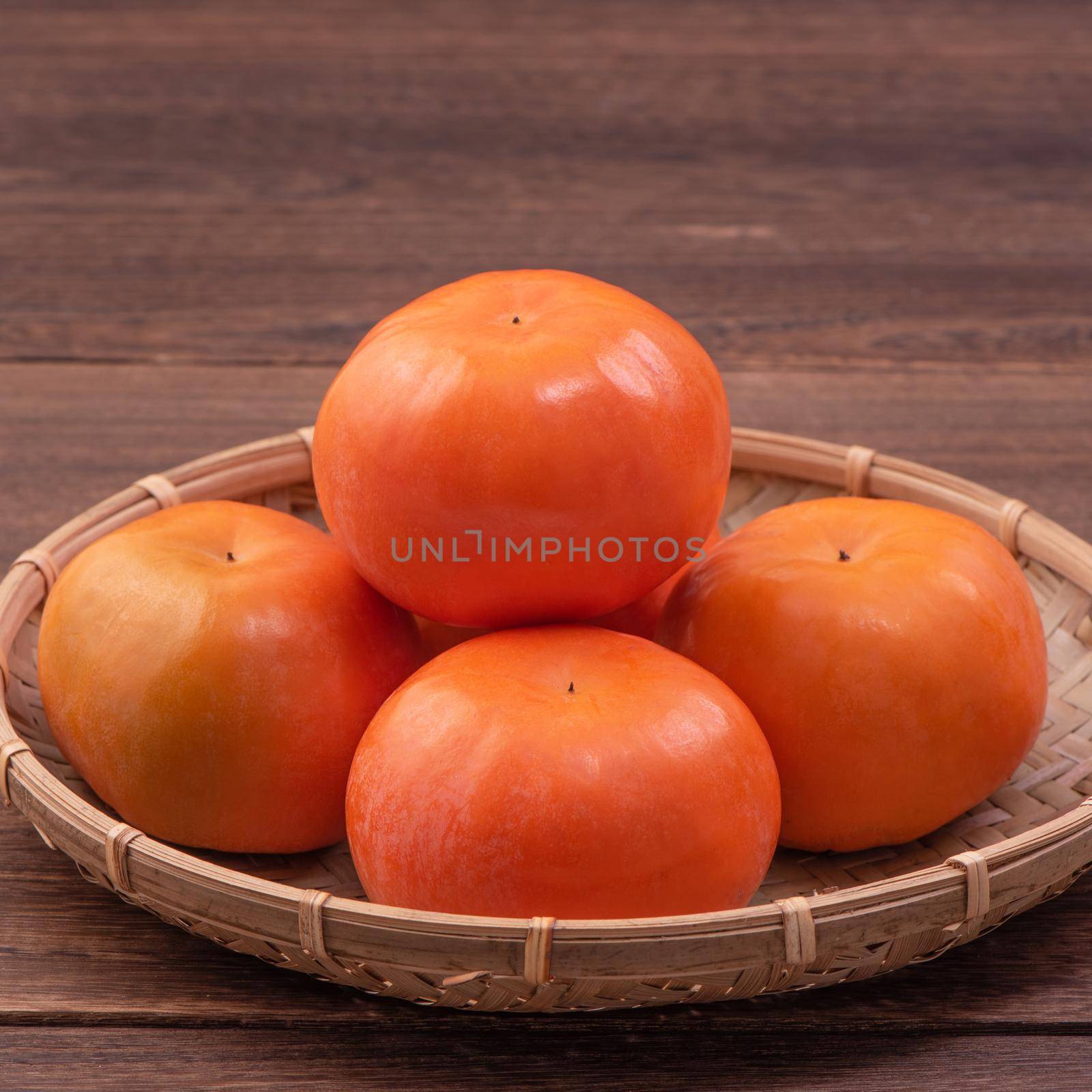 Fresh, beautiful orange color persimmon kaki on bamboo sieve over dark wooden table. Seasonal, traditional fruit of Chinese lunar new year, close up.