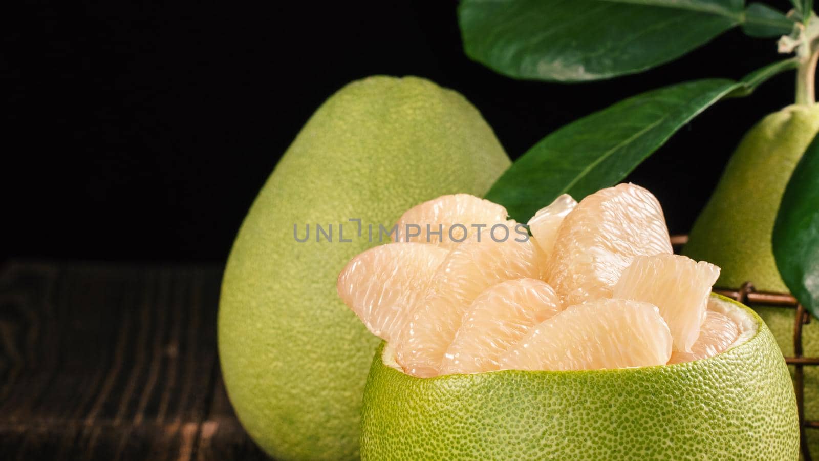 Fresh peeled pomelo, grapefruit, shaddock with green leaves on dark wooden plank table. Seasonal fruit near mid-autumn festival, close up, copy space