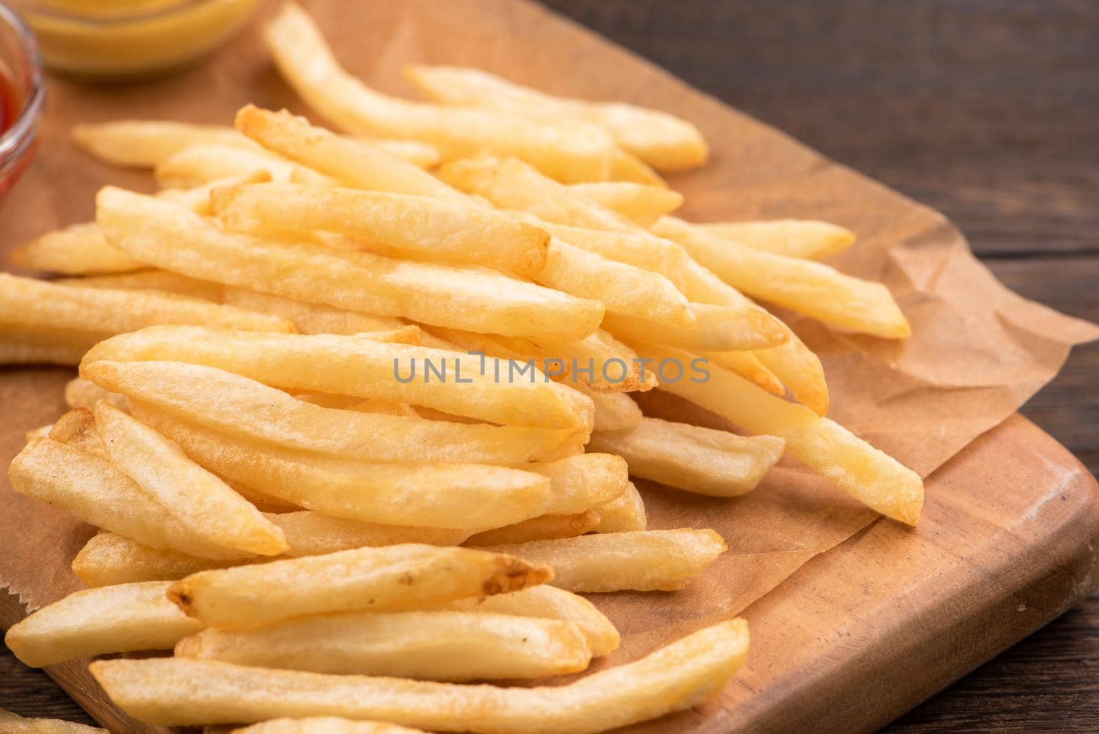 Golden yummy deep French fries on kraft baking sheet paper and serving tray to eat with ketchup and yellow mustard, top view, lifestyle.