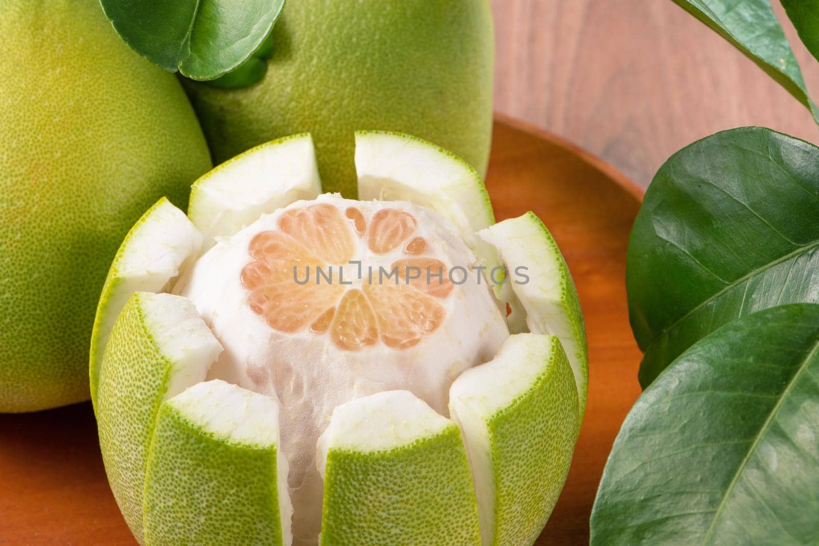 Fresh peeled pomelo, grapefruit, shaddock with green leaves on dark wooden plank table. Seasonal fruit near mid-autumn festival, close up, copy space