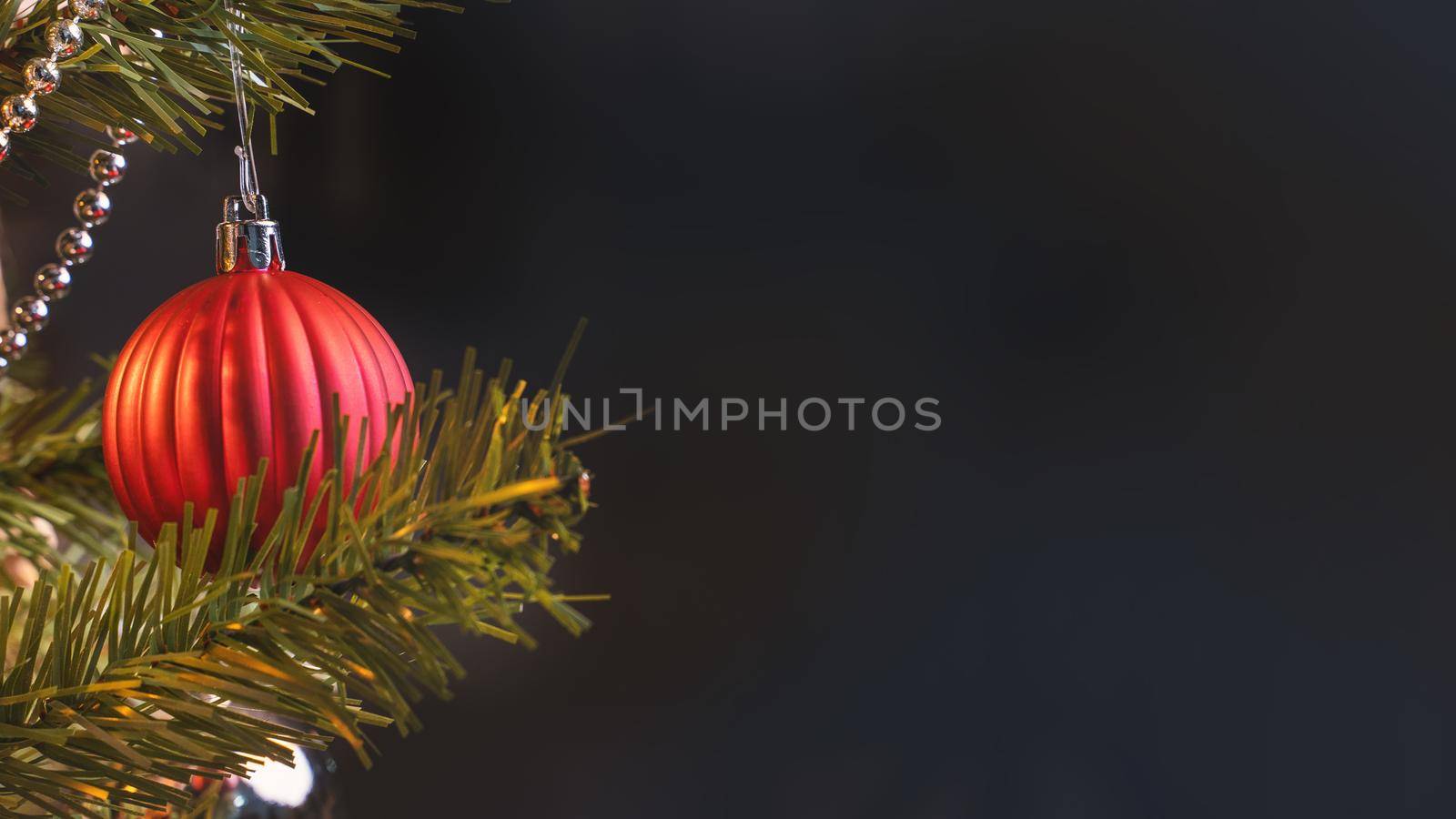 Beautiful Christmas decor concept, bauble hanging on the Christmas tree with sparkling light spot, blurry dark black background, macro detail, close up.