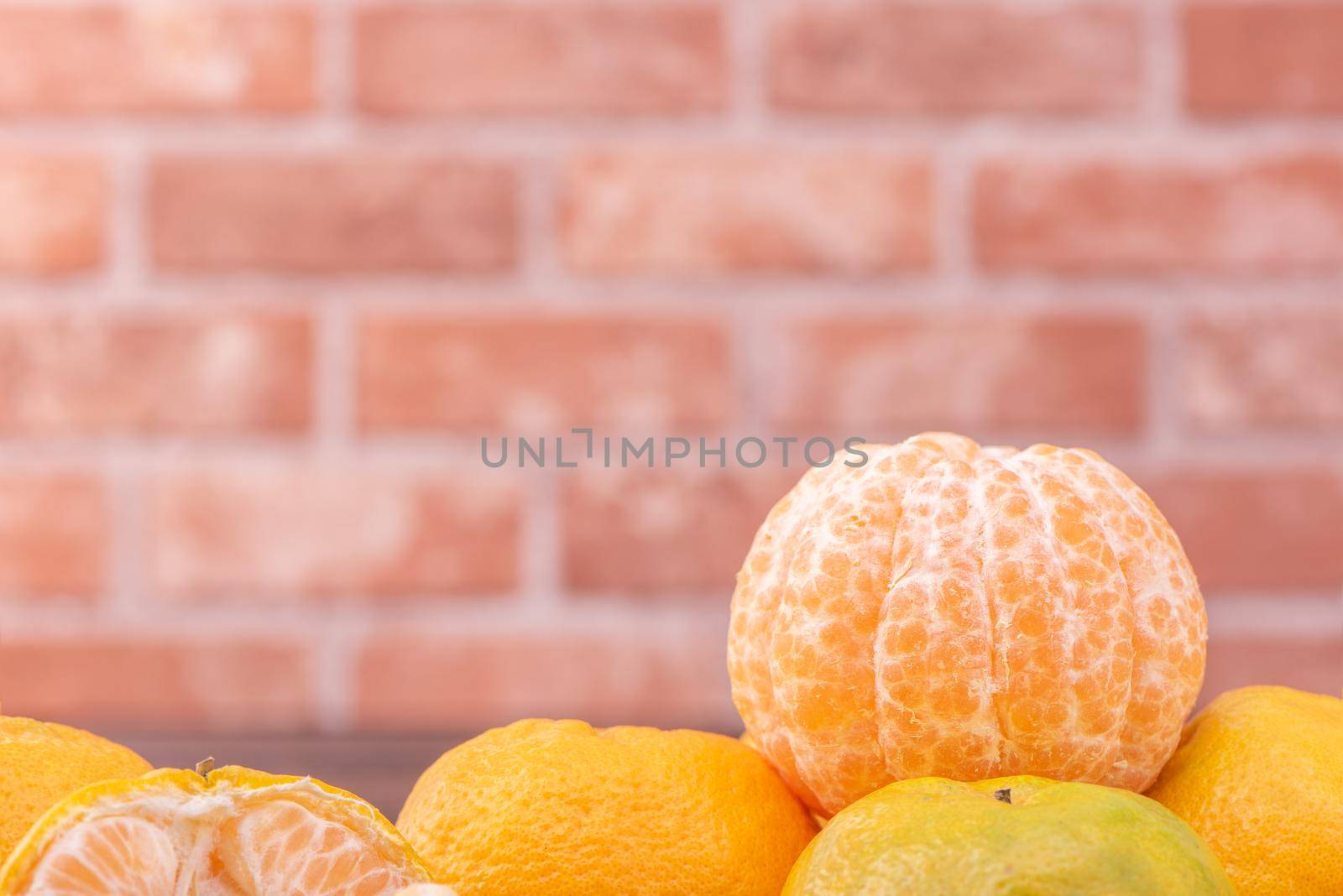 Peeled tangerines in a bamboo sieve basket on dark wooden table with red brick wall background, Chinese lunar new year fruit design concept, close up.