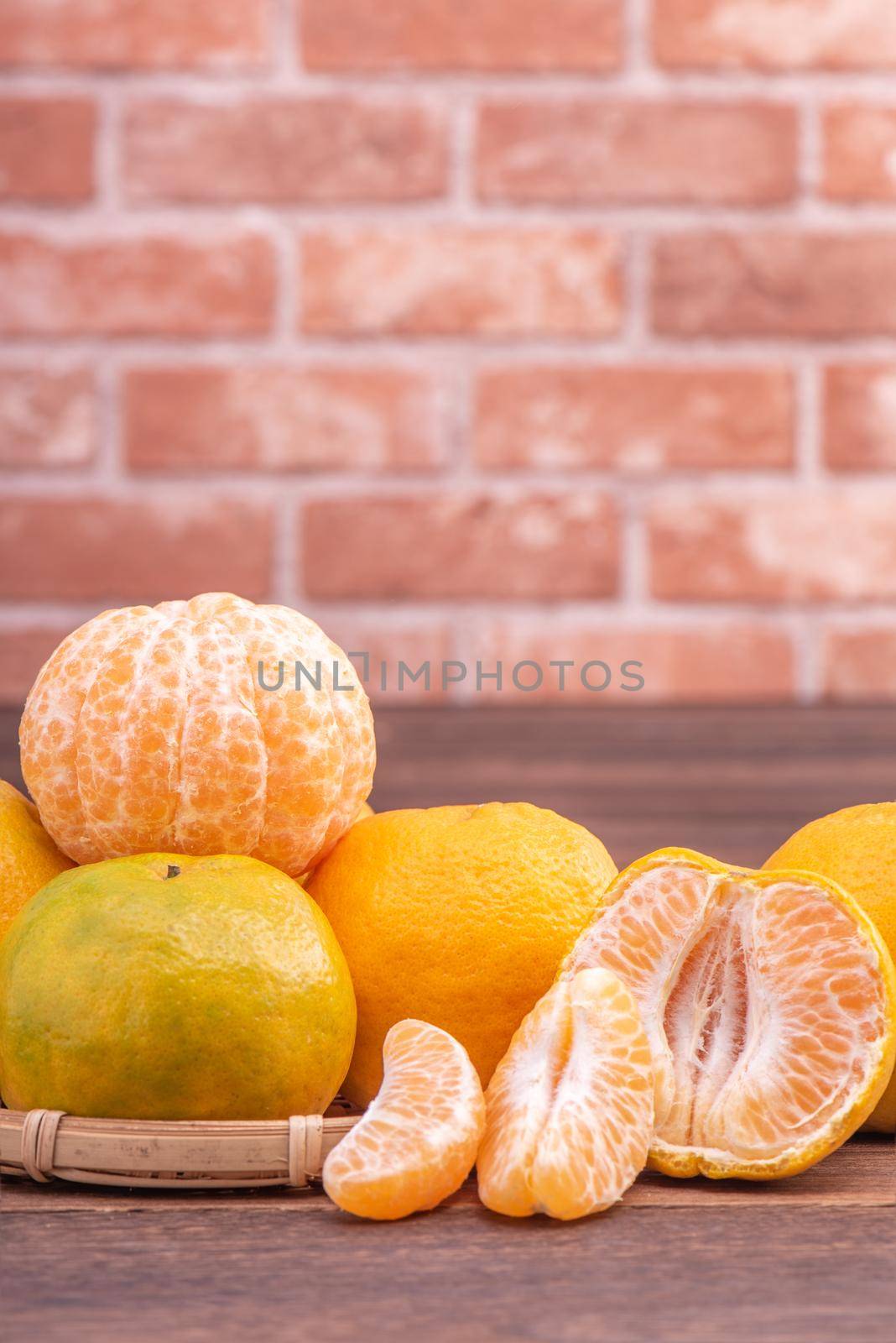 Peeled tangerines in a bamboo sieve basket on dark wooden table with red brick wall background, Chinese lunar new year fruit design concept, close up.