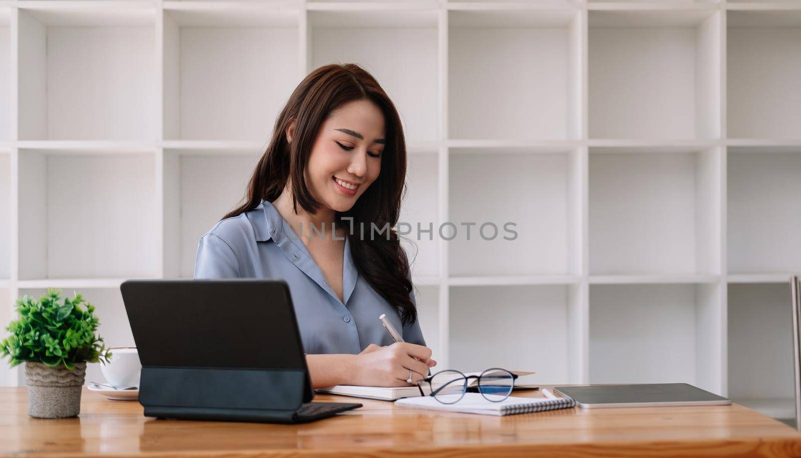 business asian woman hand taking notes with various items placed on the office table. online meeting, online learning concept.