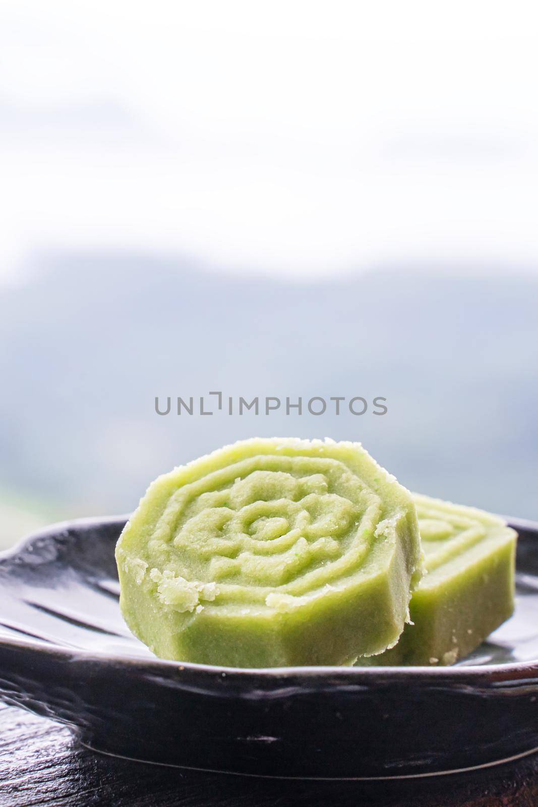 Delicious green mung bean cake with black tea plate on wooden railing of a teahouse in Taiwan with beautiful landscape in background, close up.