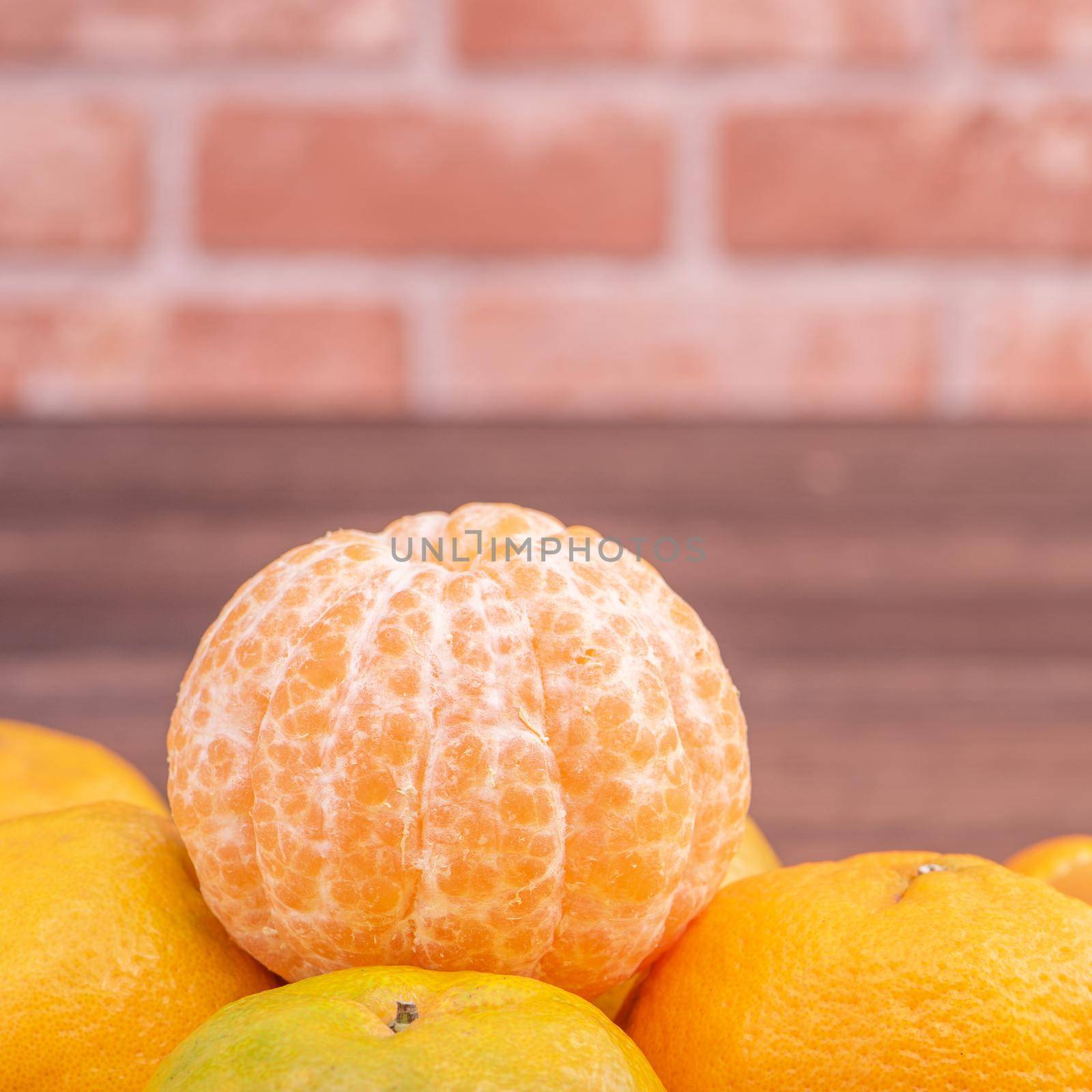 Peeled tangerines in a bamboo sieve basket on dark wooden table with red brick wall background, Chinese lunar new year fruit design concept, close up.