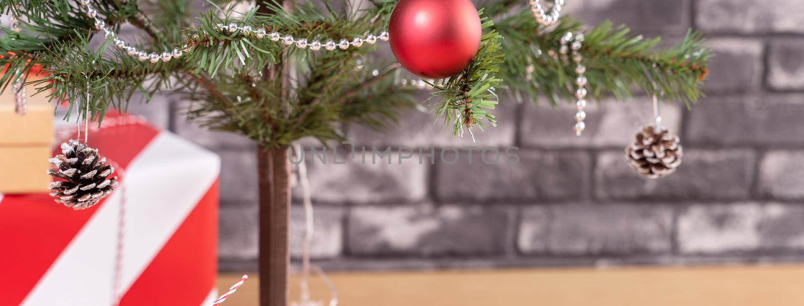 Decorated Christmas tree with wrapped beautiful red and white gifts at home with black brick wall, festive design concept, close up.