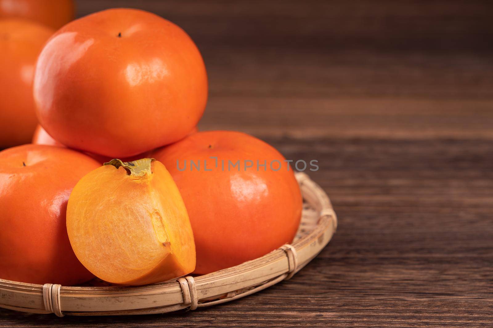 Fresh, beautiful orange color persimmon kaki on bamboo sieve over dark wooden table. Seasonal, traditional fruit of Chinese lunar new year, close up.