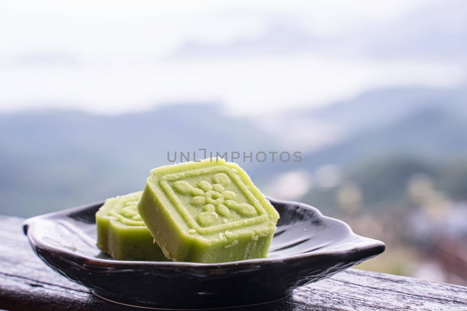 Delicious green mung bean cake with black tea plate on wooden railing of a teahouse in Taiwan with beautiful landscape in background, close up.