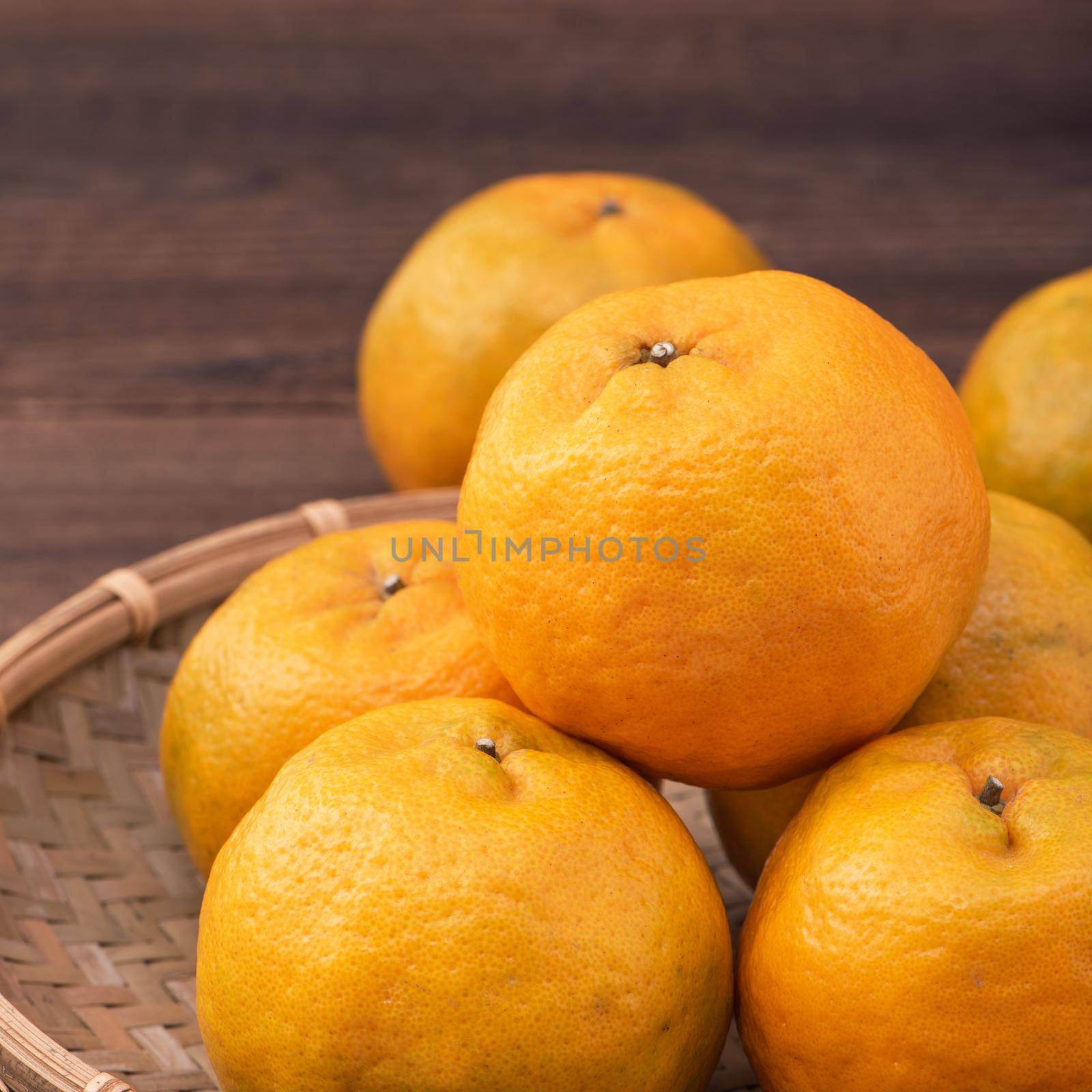 Fresh, beautiful orange color tangerine on bamboo sieve over dark wooden table. Seasonal, traditional fruit of Chinese lunar new year, close up. by ROMIXIMAGE