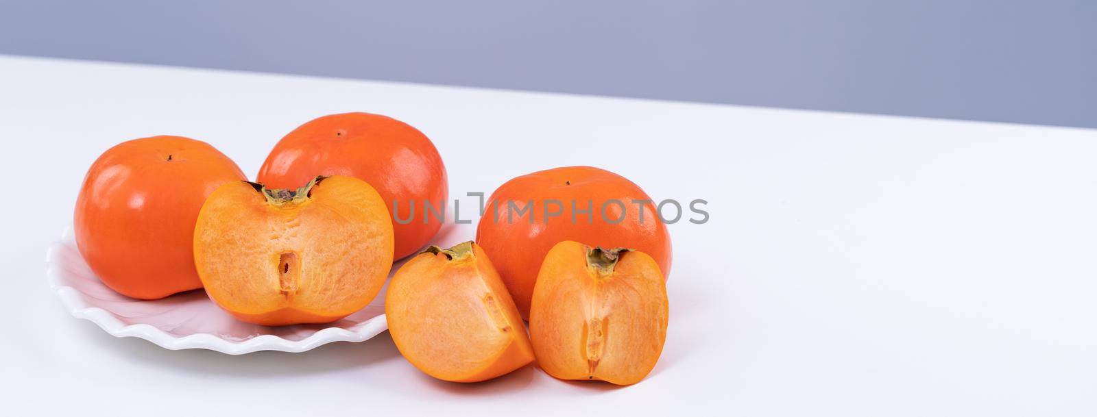 Fresh beautiful sliced sweet persimmon kaki isolated on white kitchen table with gray blue background, Chinese lunar new year design concept, close up.