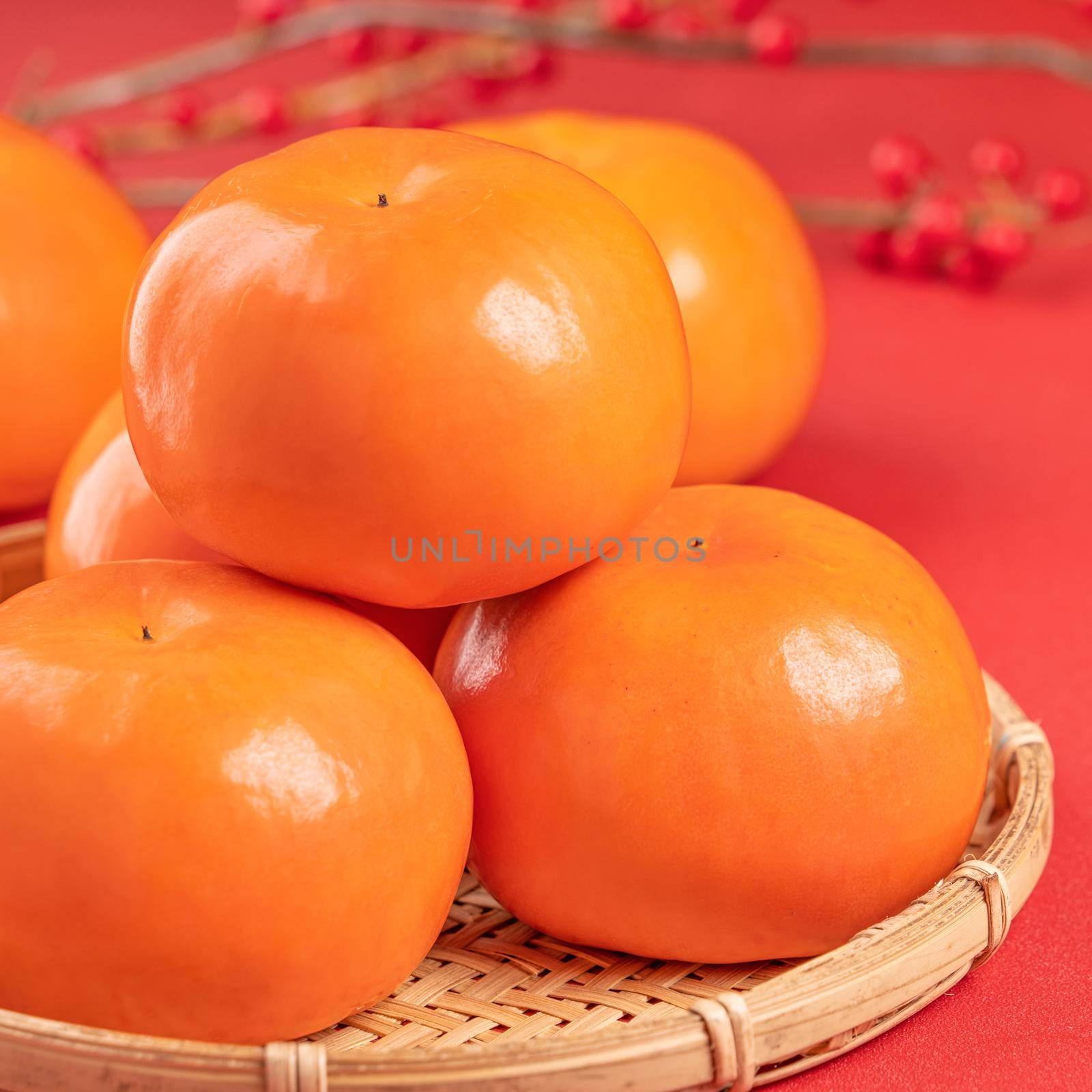 Fresh beautiful sliced sweet persimmon kaki isolated on red table background and bamboo sieve, Chinese lunar new year design concept, close up. by ROMIXIMAGE