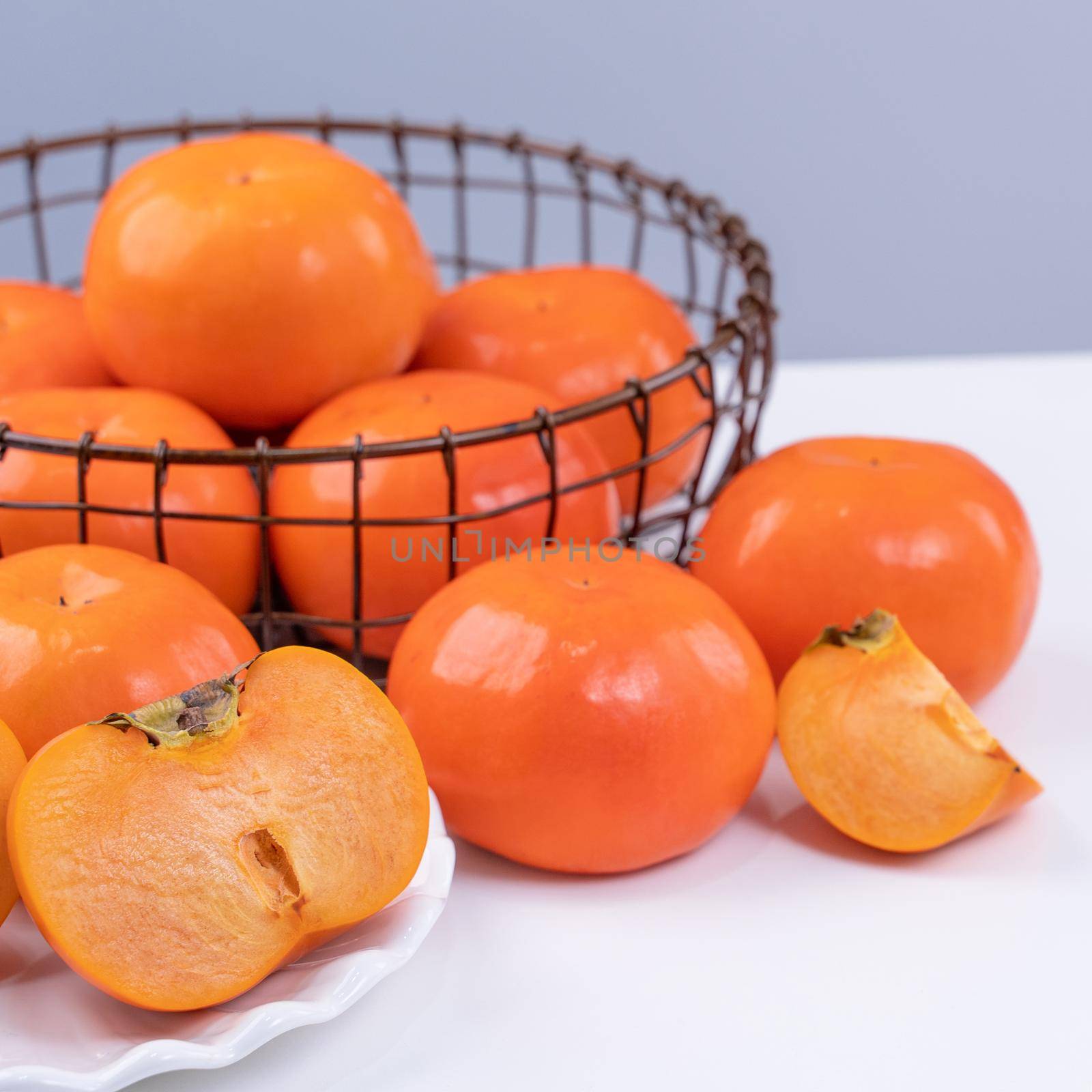 Fresh beautiful sliced sweet persimmon kaki isolated on white kitchen table with gray blue background, Chinese lunar new year design concept, close up.