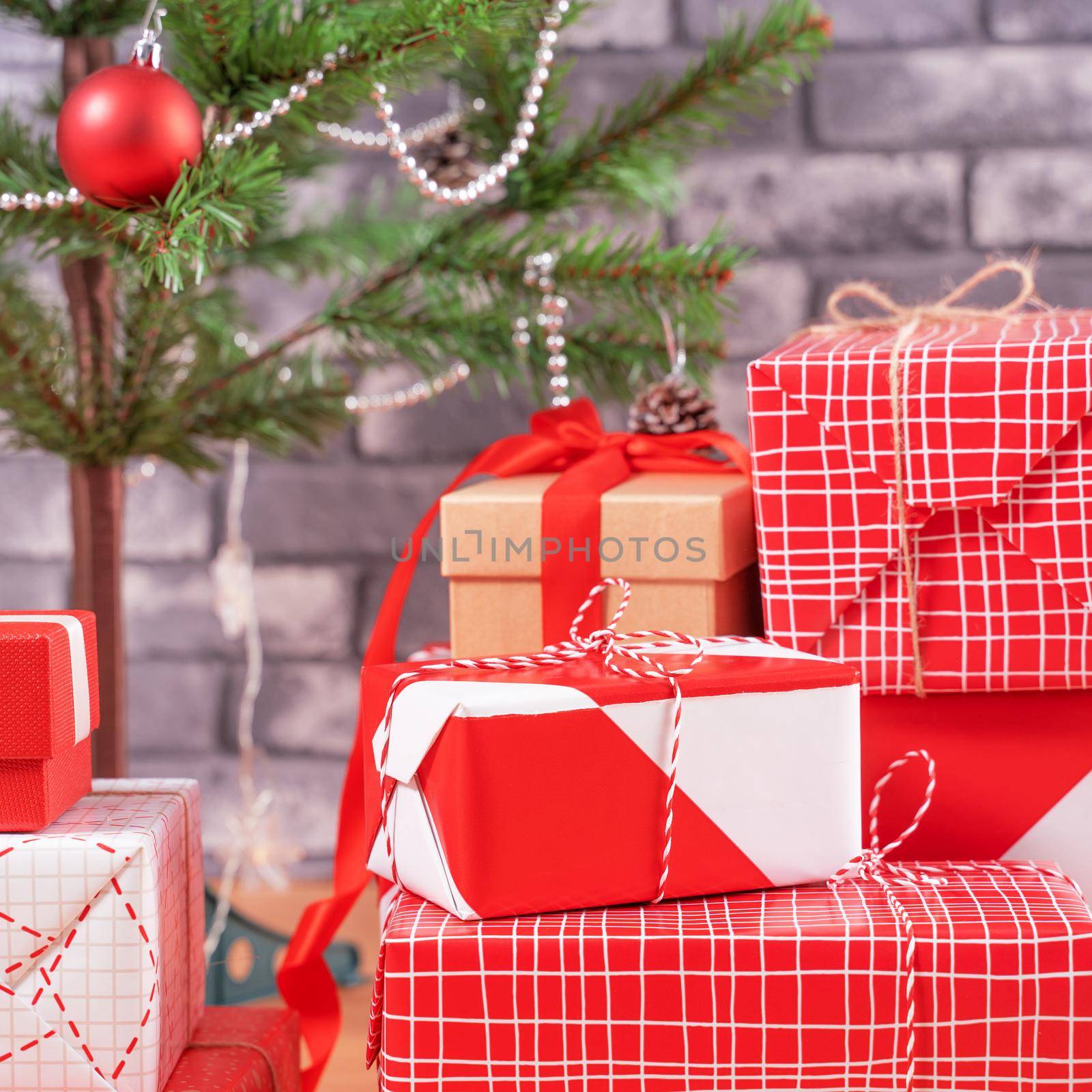 Decorated Christmas tree with wrapped beautiful red and white gifts at home with black brick wall, festive design concept, close up.