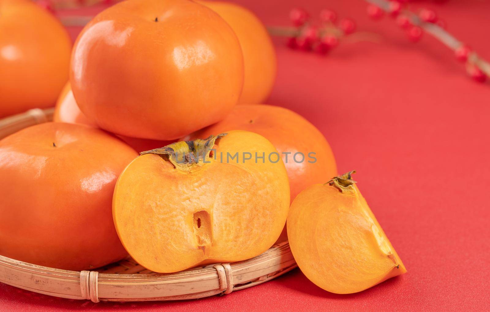 Fresh beautiful sliced sweet persimmon kaki isolated on red table background and bamboo sieve, Chinese lunar new year design concept, close up.
