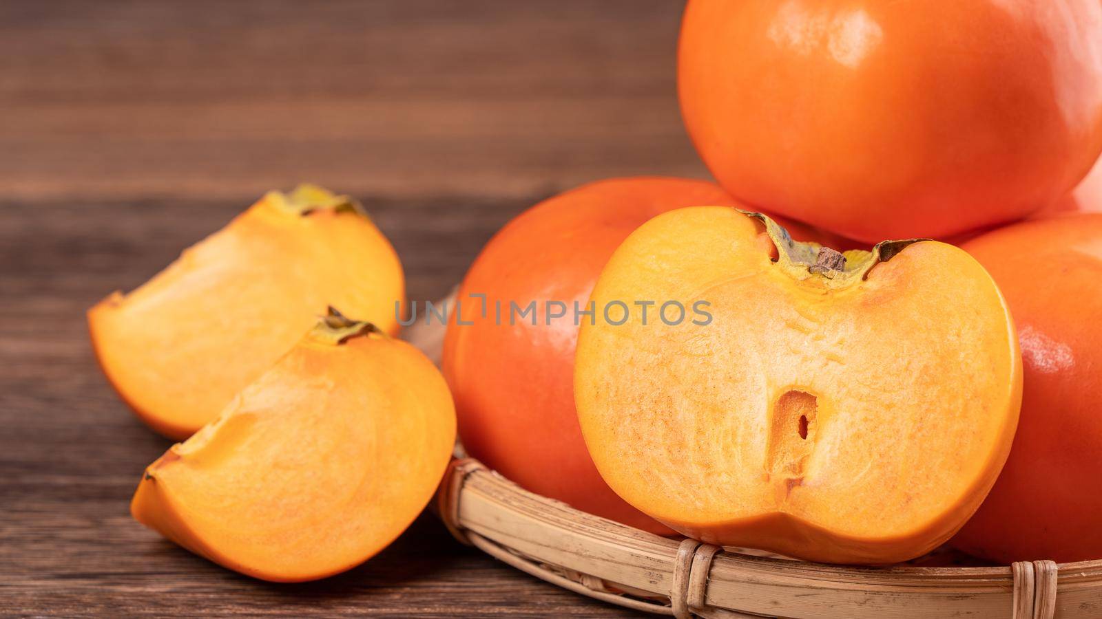 Fresh, beautiful orange color persimmon kaki on bamboo sieve over dark wooden table. Seasonal, traditional fruit of Chinese lunar new year, close up.