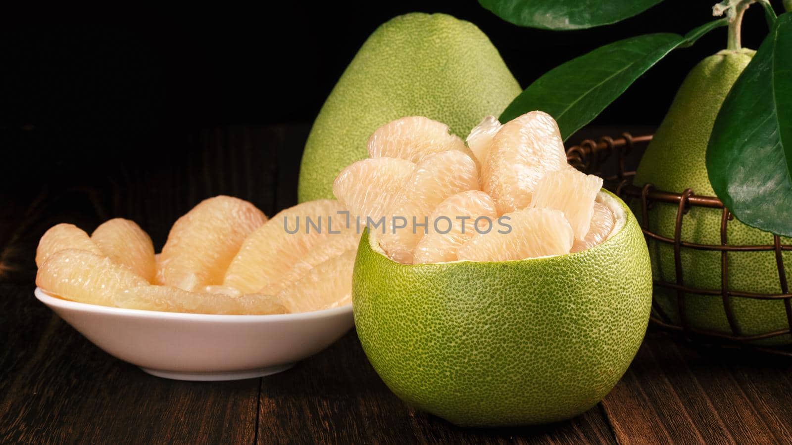 Fresh peeled pomelo, grapefruit, shaddock with green leaves on dark wooden plank table. Seasonal fruit near mid-autumn festival, close up, copy space