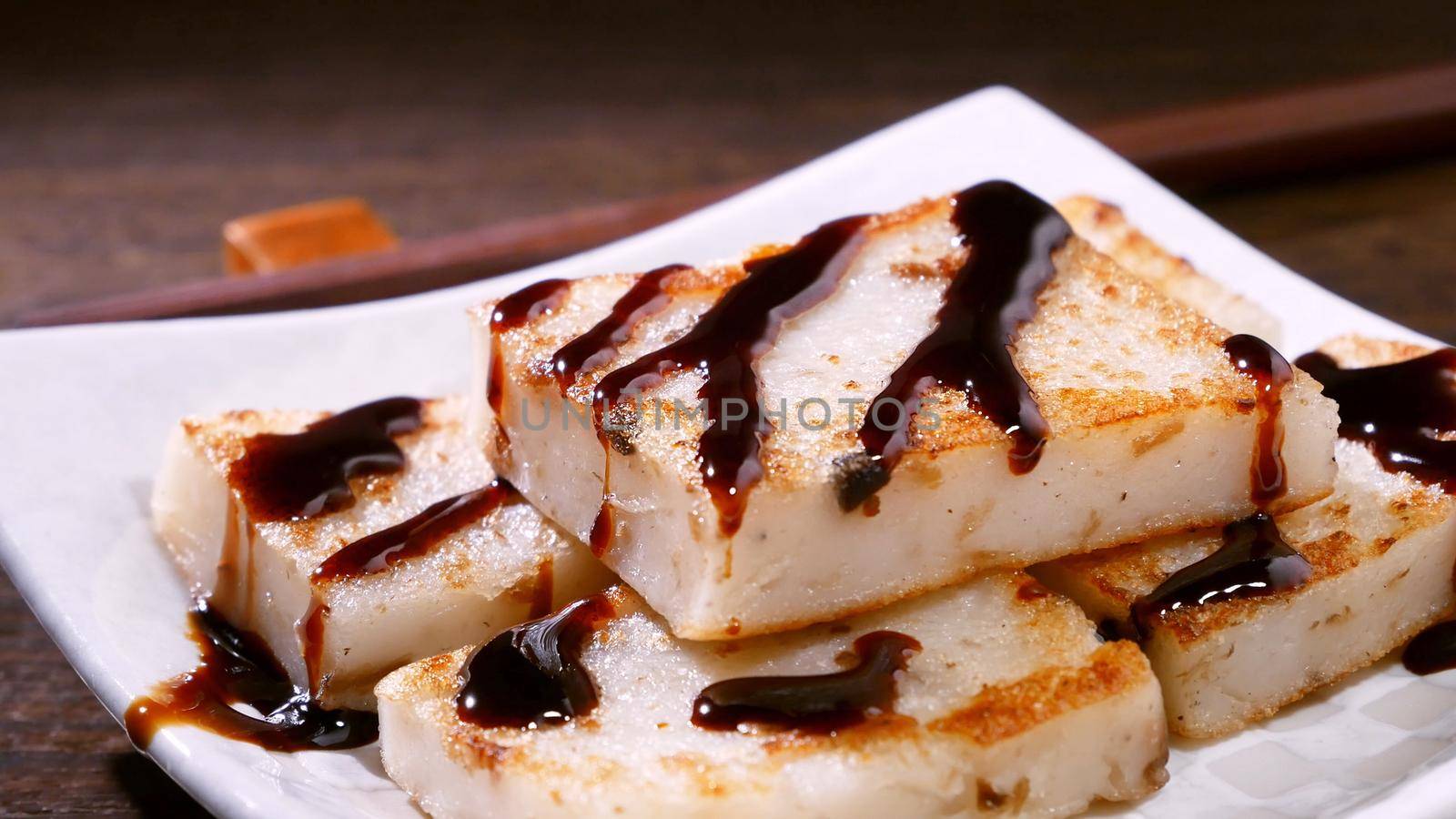 Pouring black soy sauce on ready-to-eat delicious turnip cake, Chinese traditional local dish radish cake in restaurant, close up, copy space.