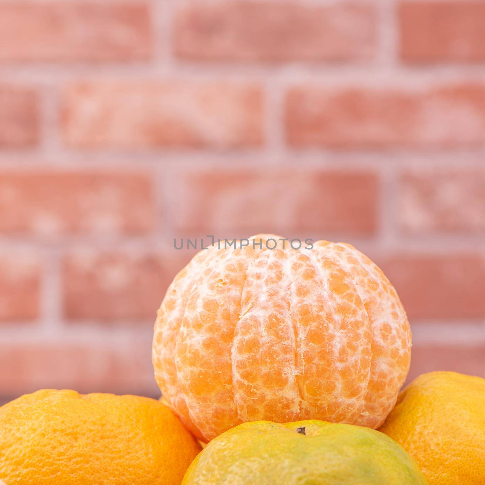 Peeled tangerines in a bamboo sieve basket on dark wooden table with red brick wall background, Chinese lunar new year fruit design concept, close up.