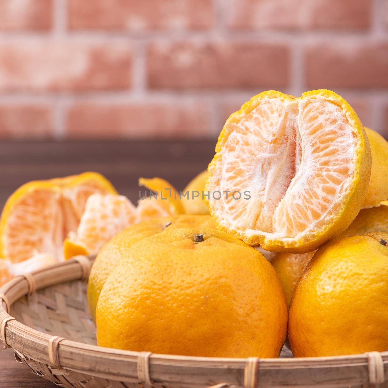 Peeled tangerines in a bamboo sieve basket on dark wooden table with red brick wall background, Chinese lunar new year fruit design concept, close up. by ROMIXIMAGE