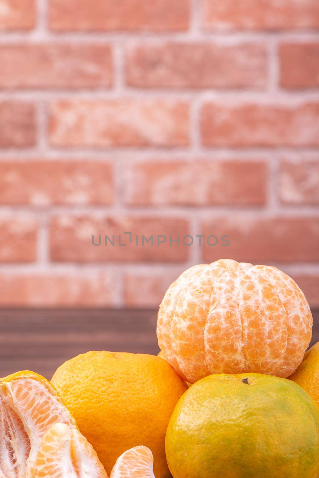 Peeled tangerines in a bamboo sieve basket on dark wooden table with red brick wall background, Chinese lunar new year fruit design concept, close up.