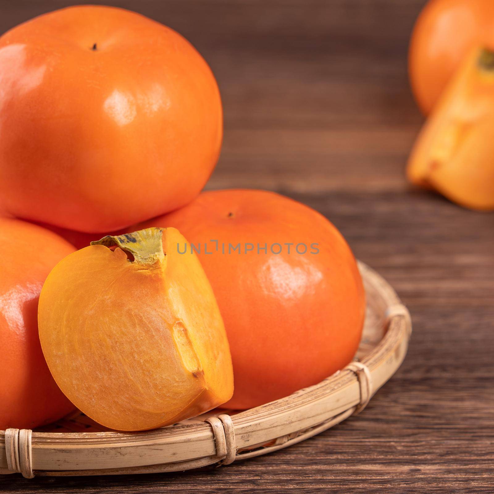 Fresh, beautiful orange color persimmon kaki on bamboo sieve over dark wooden table. Seasonal, traditional fruit of Chinese lunar new year, close up. by ROMIXIMAGE