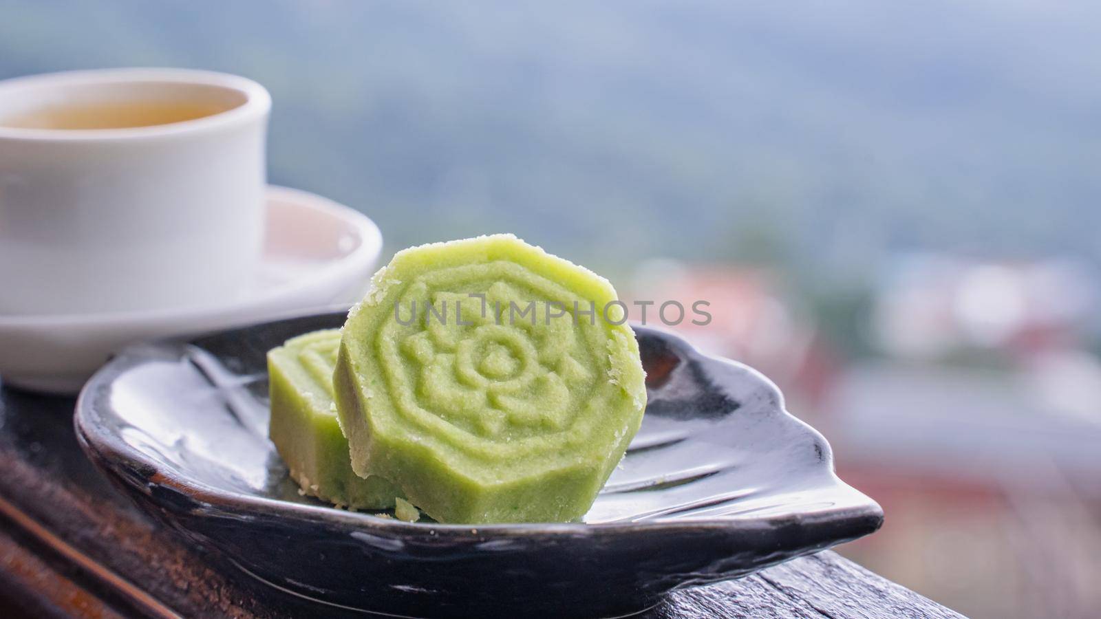 Delicious green mung bean cake with black tea plate on wooden railing of a teahouse in Taiwan with beautiful landscape in background, close up.