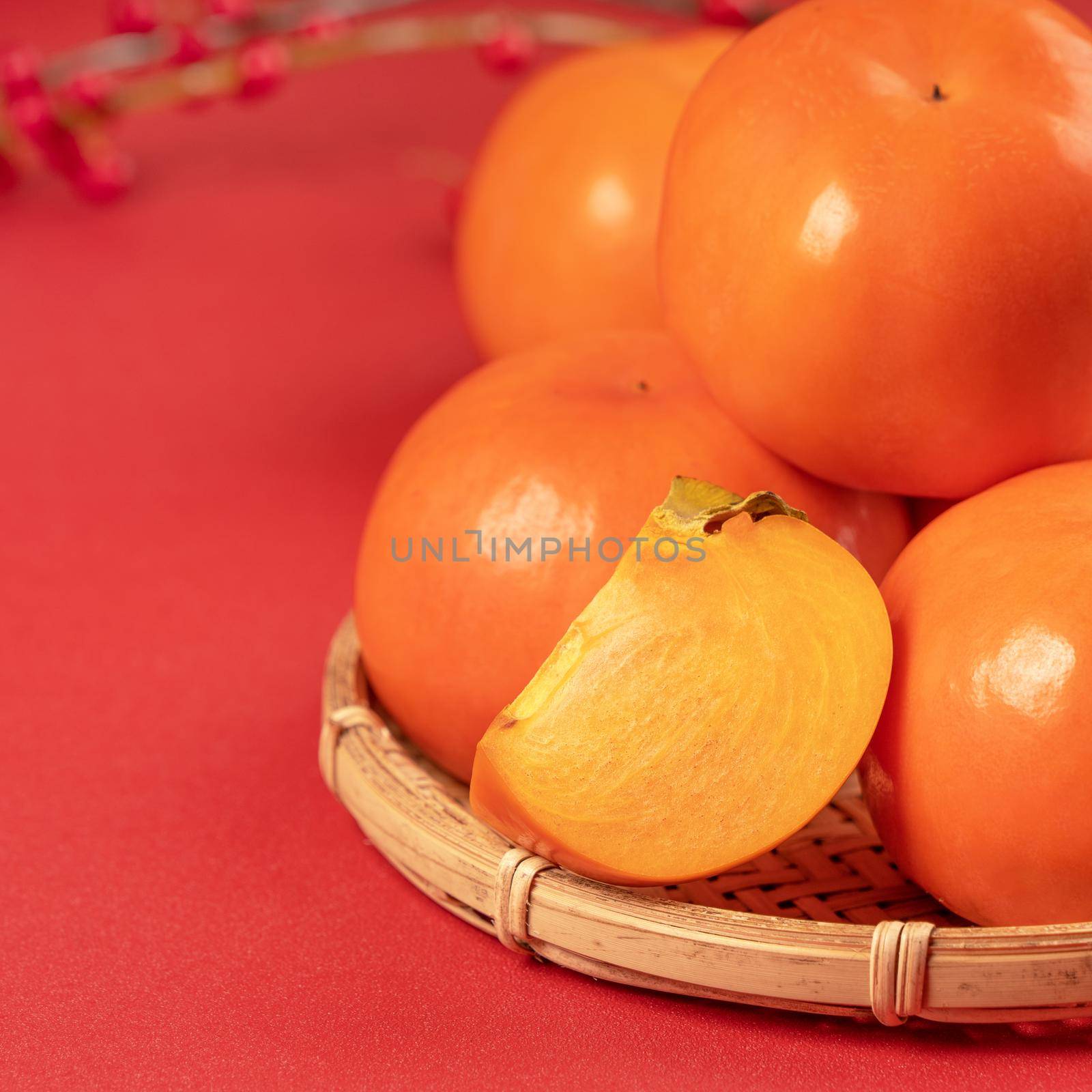 Fresh beautiful sliced sweet persimmon kaki isolated on red table background and bamboo sieve, Chinese lunar new year design concept, close up. by ROMIXIMAGE