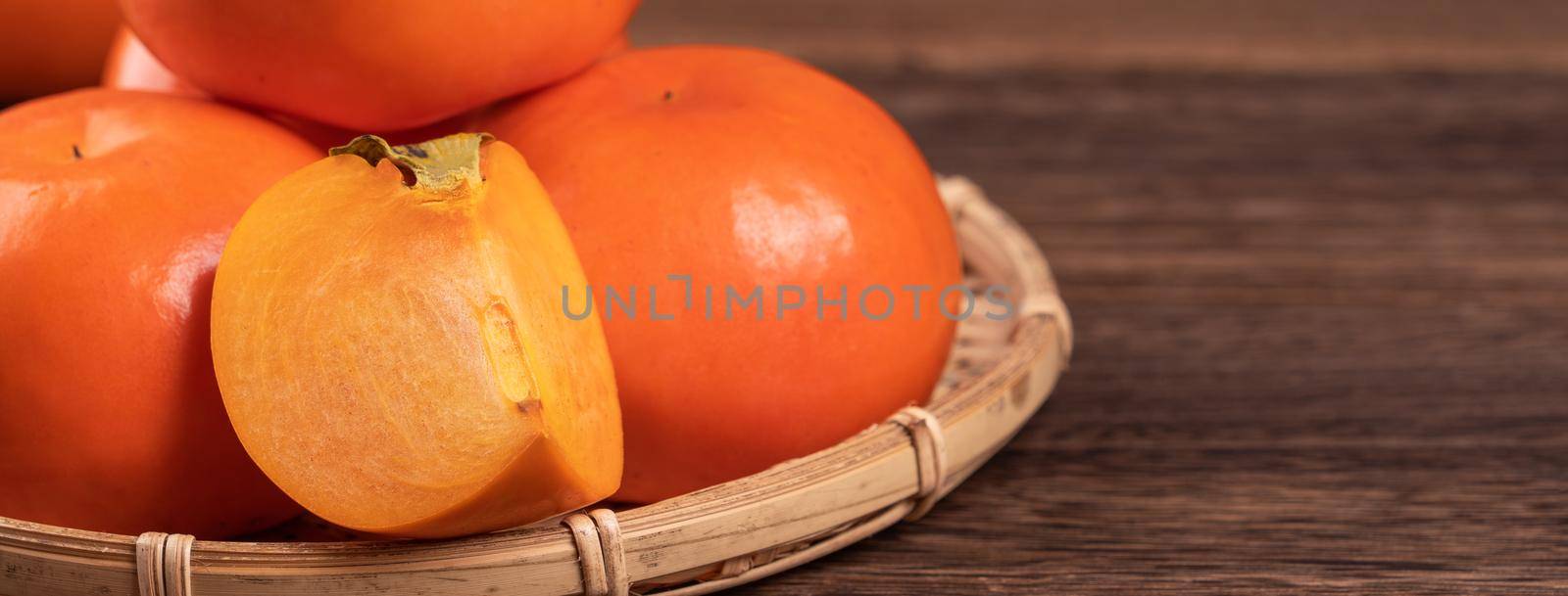 Fresh, beautiful orange color persimmon kaki on bamboo sieve over dark wooden table. Seasonal, traditional fruit of Chinese lunar new year, close up. by ROMIXIMAGE