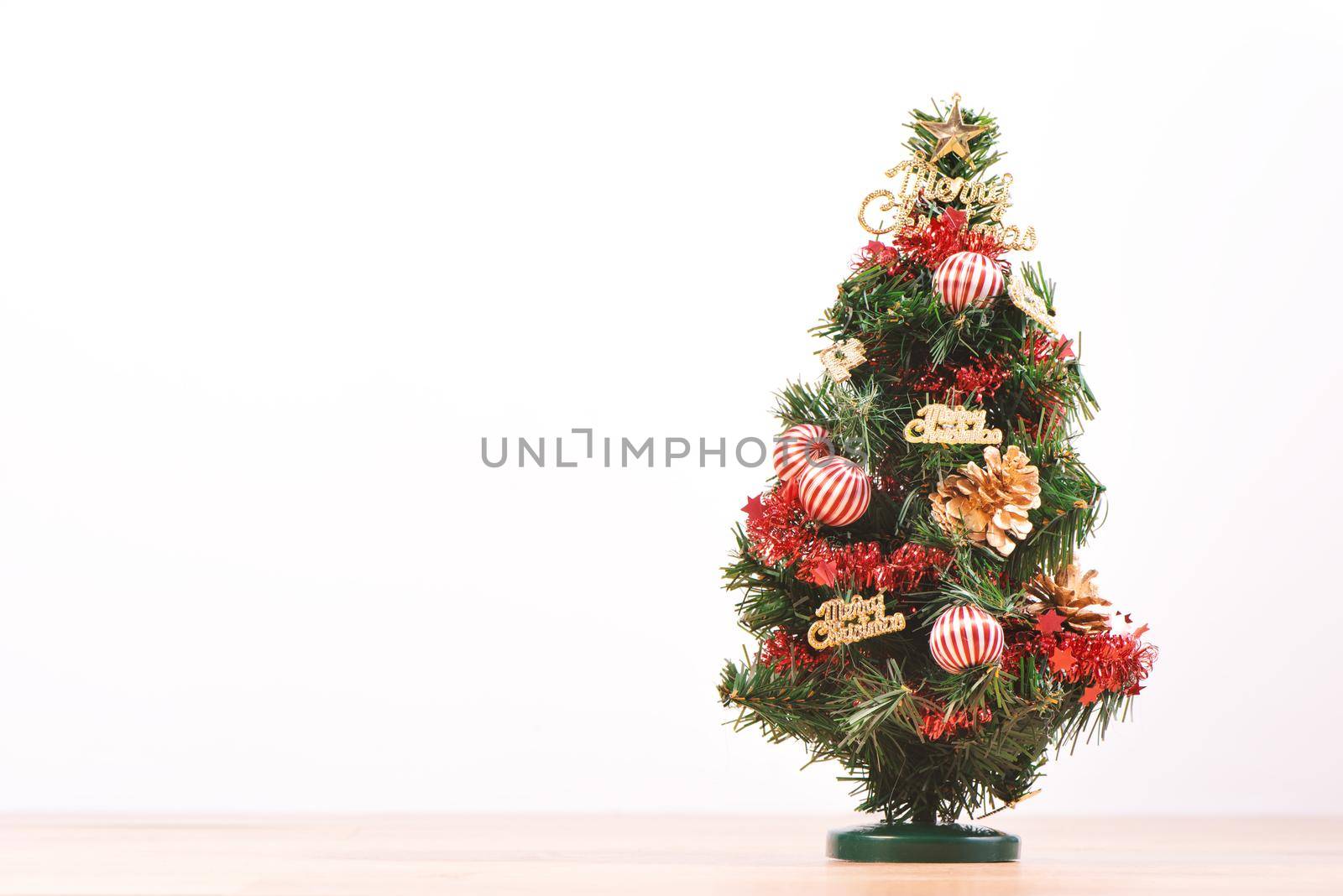 Decorated cute Christmas tree on a wooden floor with white background and toys, blank for festive design concept, close up.