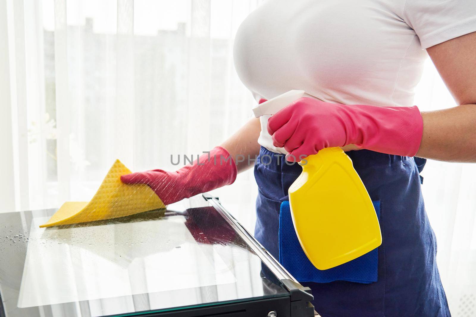 Young woman cleaning oven in kitchen. Cleaning service concept