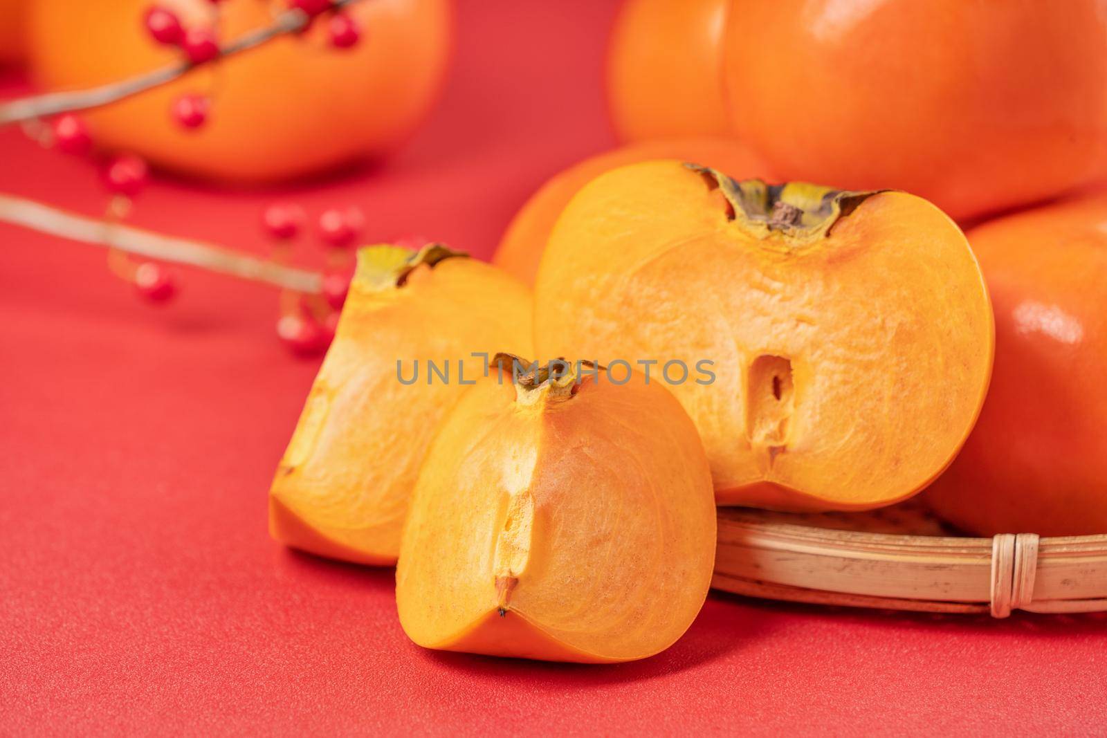 Fresh beautiful sliced sweet persimmon kaki isolated on red table background and bamboo sieve, Chinese lunar new year design concept, close up.