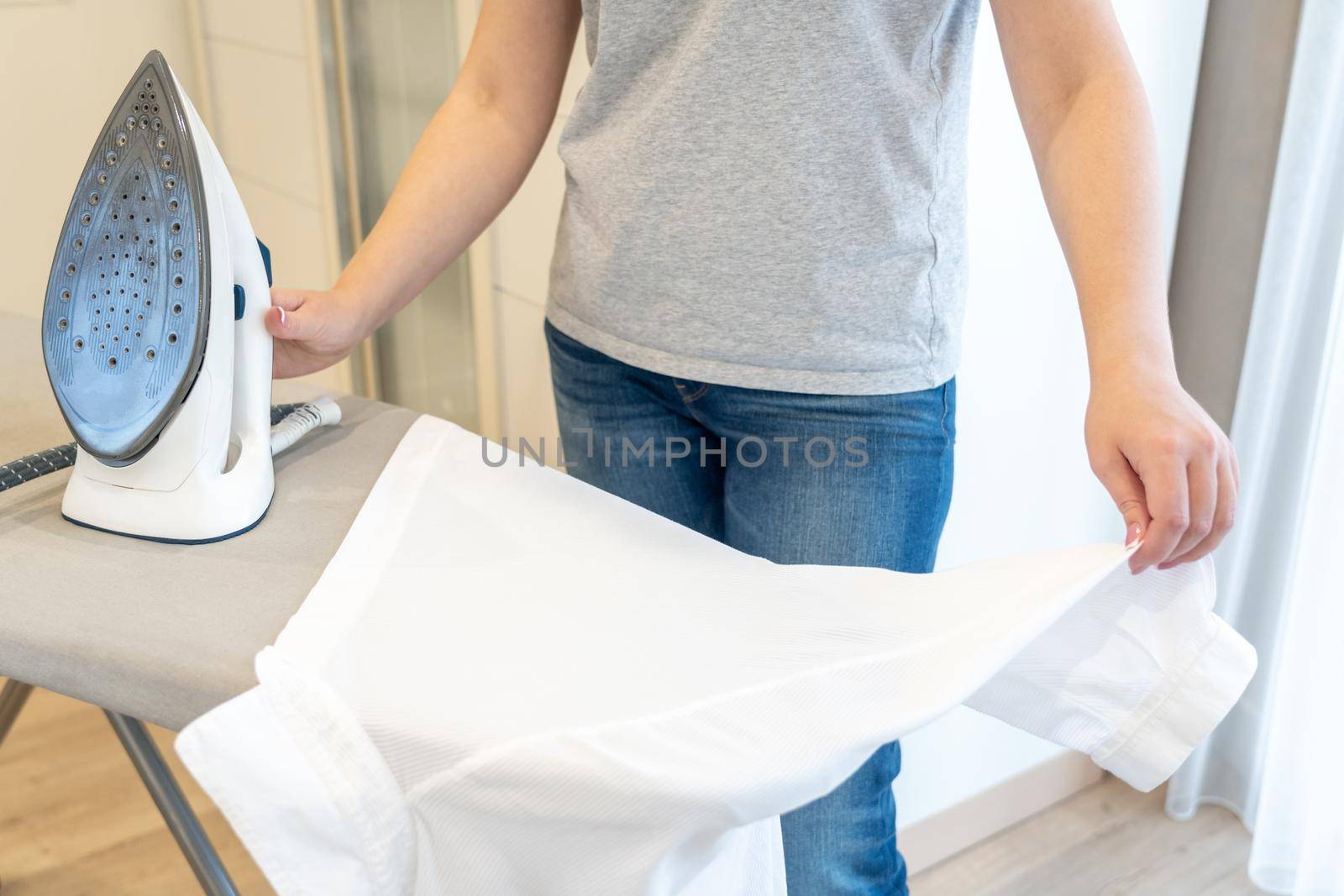 Woman ironing sleeve of white shirt with much steam on ironing board