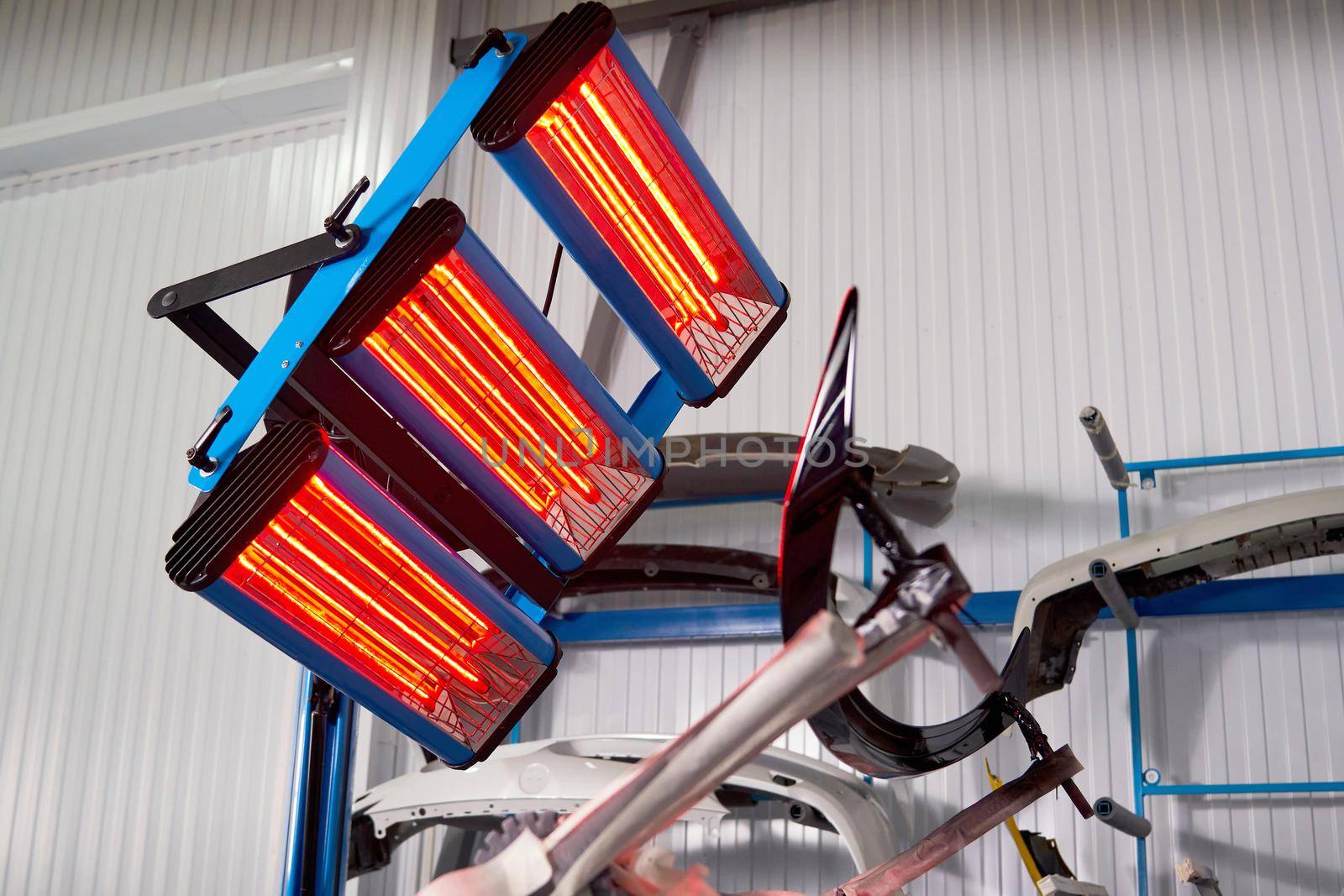 Painting and drying under lamps in professional box of car body parts after applying paint on bumper