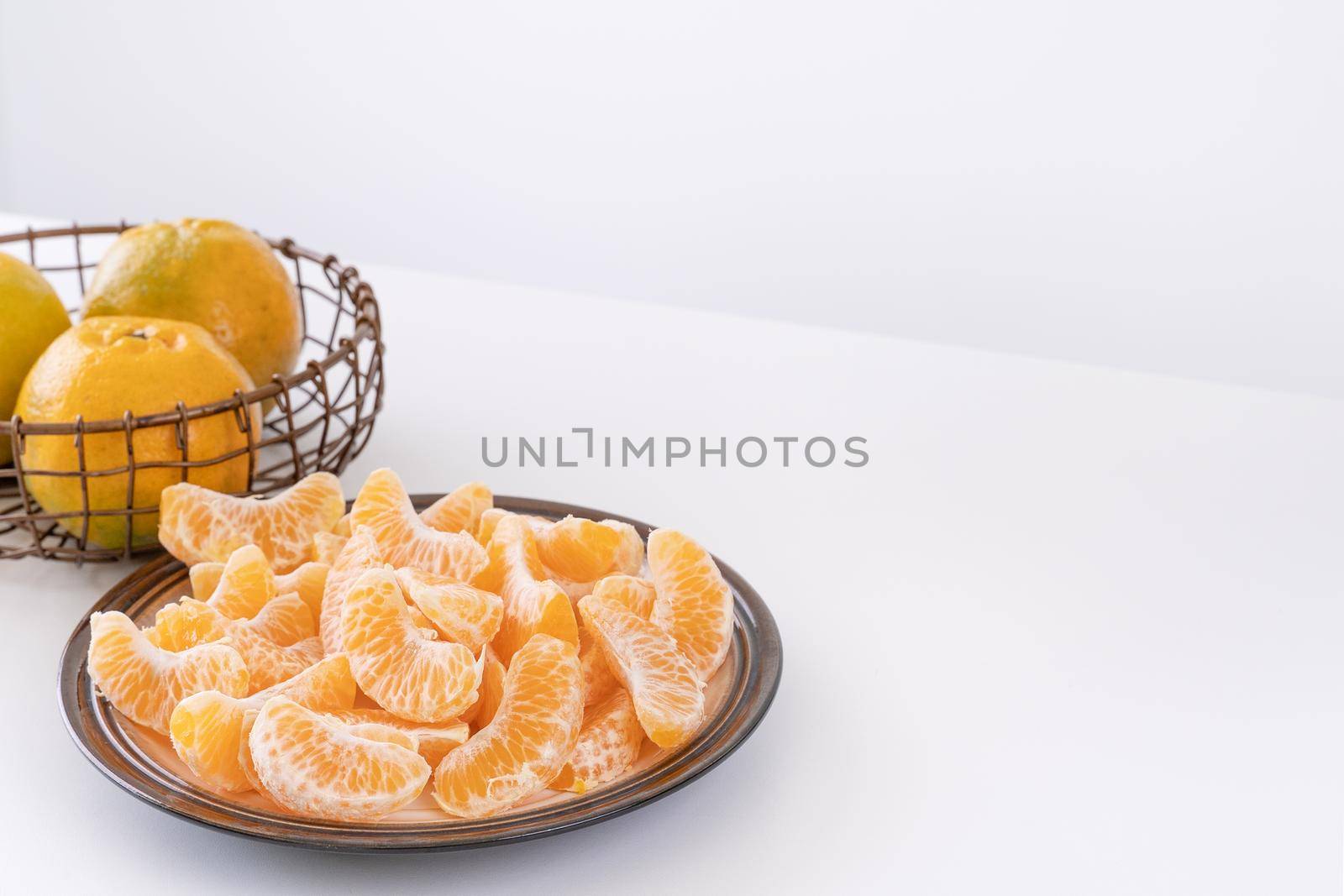 Beautiful peeled tangerines in a plate and metal basket isolated on bright white clean table in a modern contemporary kitchen island, close up.