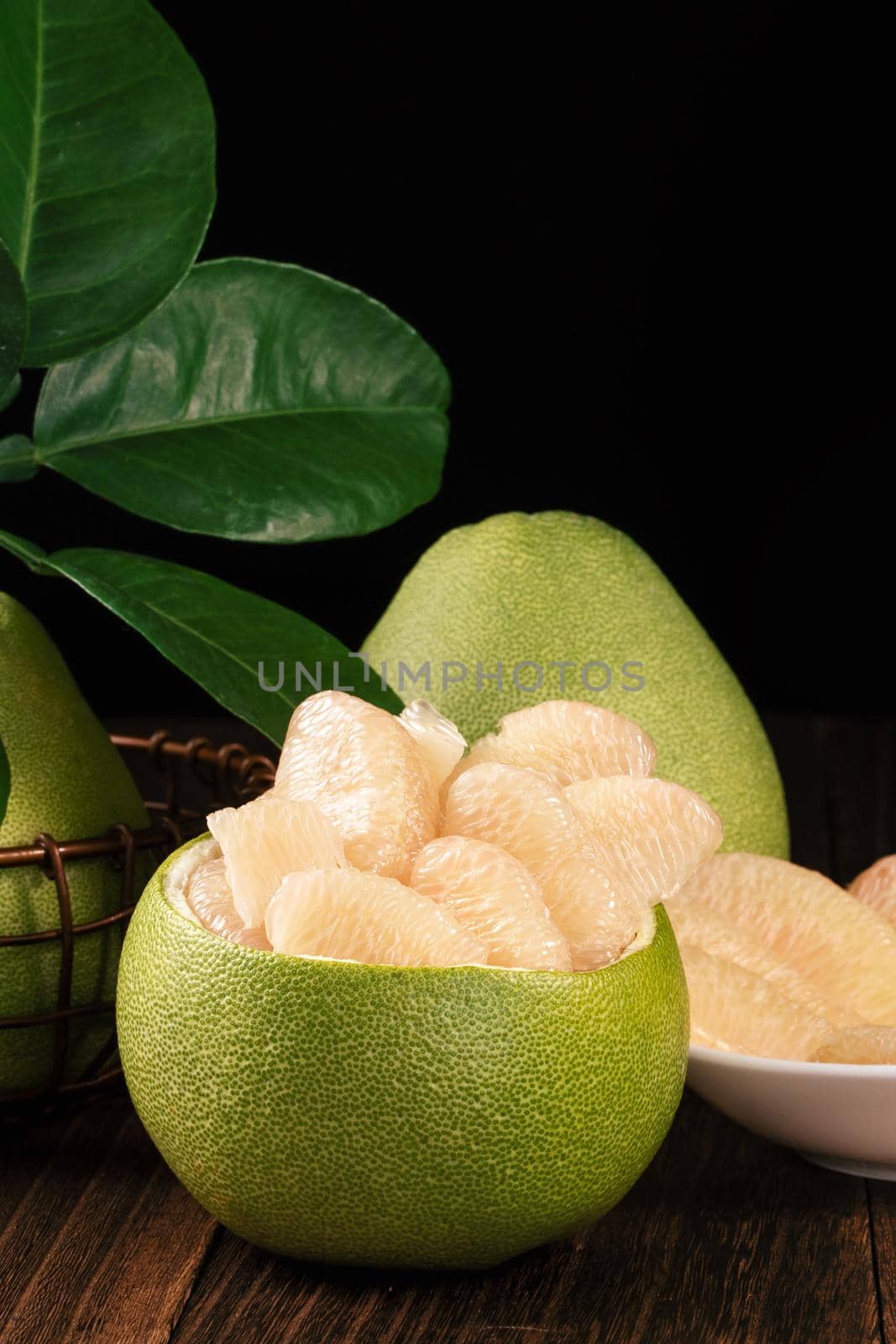 Fresh peeled pomelo, grapefruit, shaddock with green leaves on dark wooden plank table. Seasonal fruit near mid-autumn festival, close up, copy space