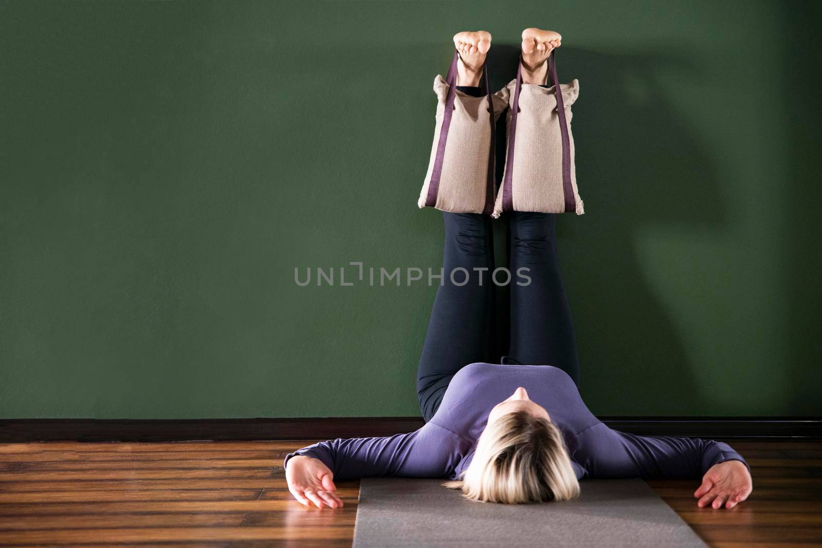Young woman in yoga relaxing pose with legs up by a wall with heavy sand bags