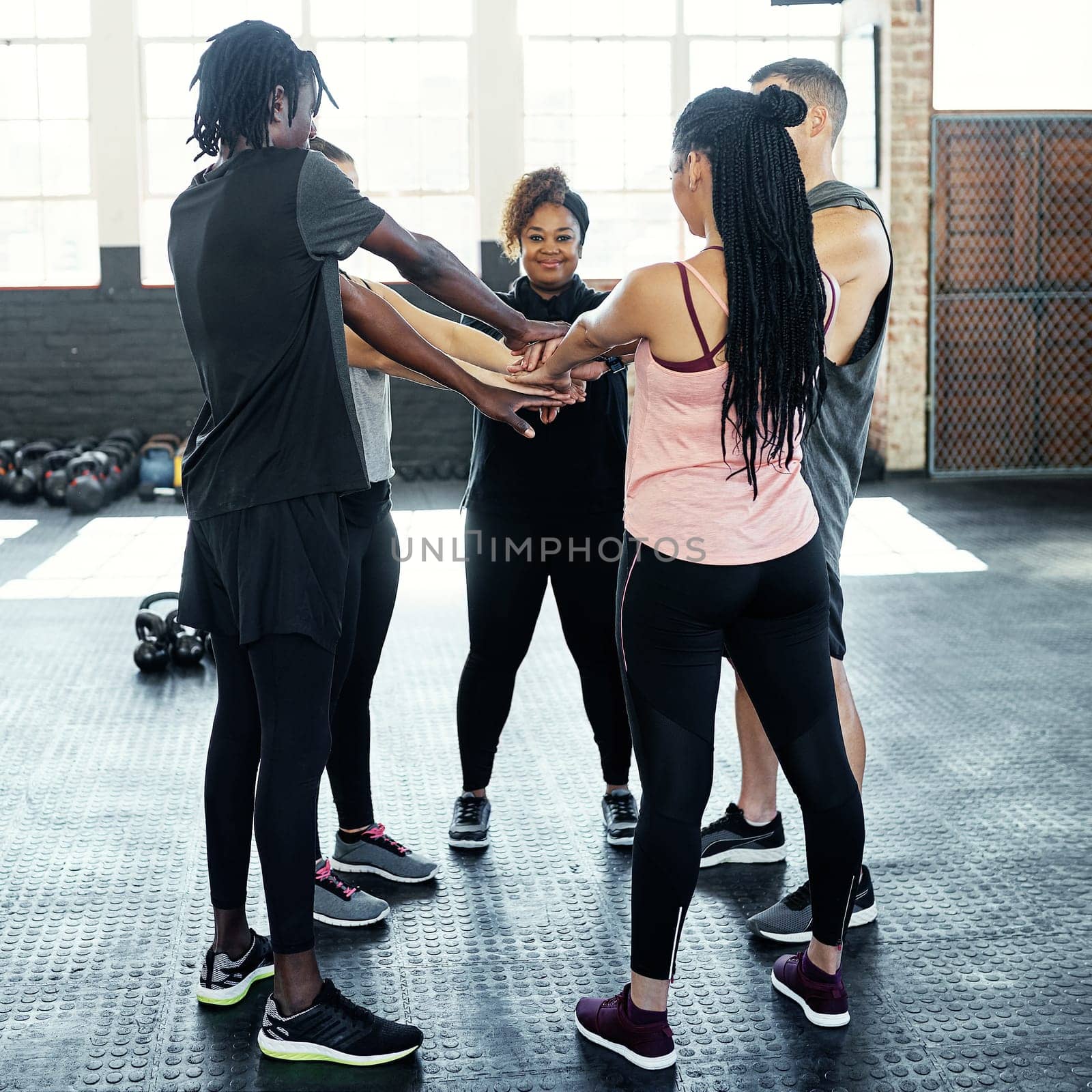 All about that fitness. a cheerful young group of people forming a huddle together while one looks at the camera before a workout session in a gym. by YuriArcurs