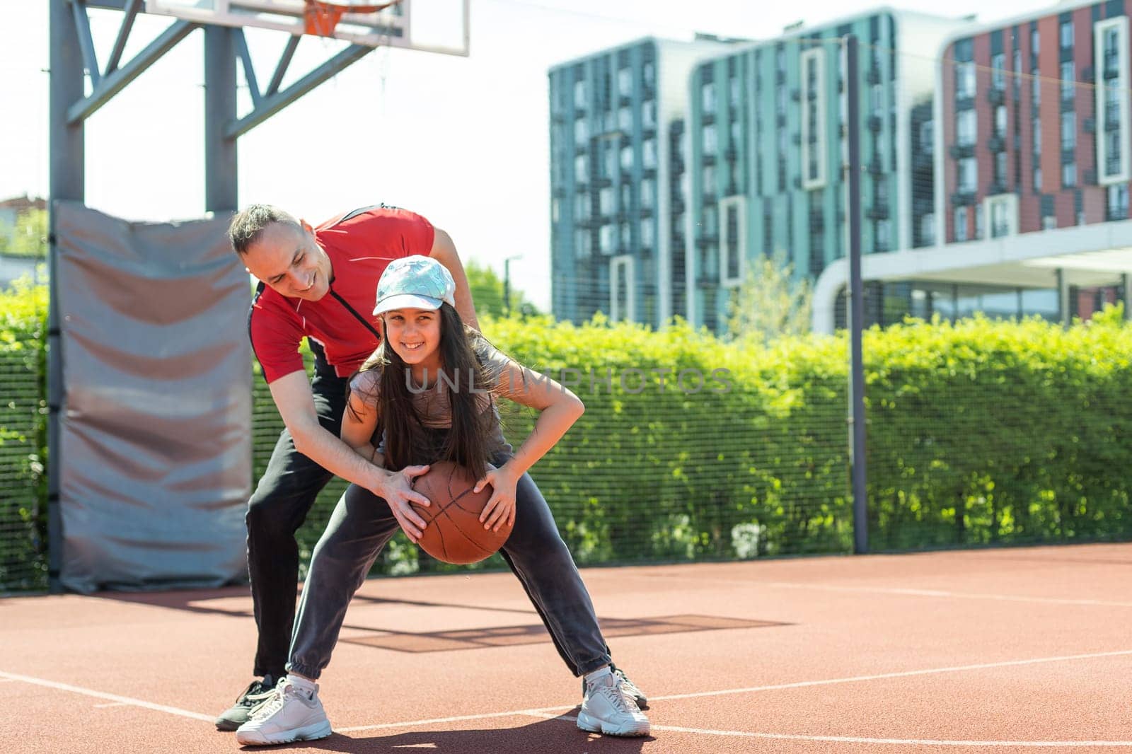 Happy father and teen daughter embracing and looking at camera outside at basketball court