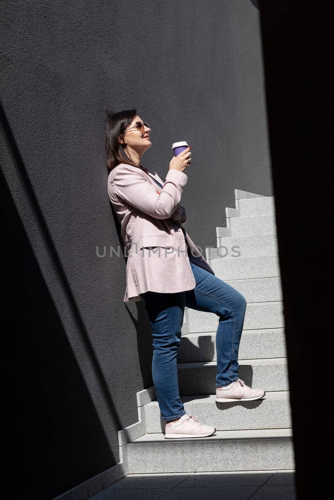 Beautiful Brunette Woman Drinks Coffee From Paper Cup, Standing On Stairs Near Office Outdoor, Dressed In Stylish Casual Clothes, Summer Sunny Day. Taking A Break. Lifestyle Mature Female. Vertical.