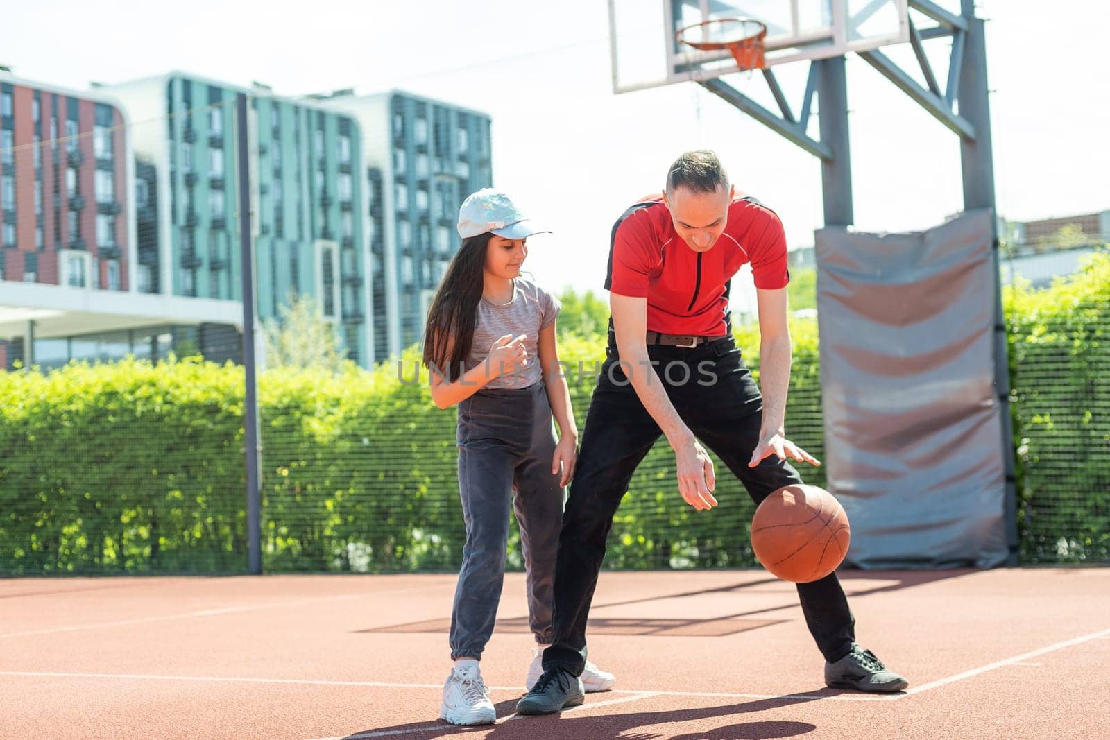 Happy father and teenage daughter playing basketball outside at court.