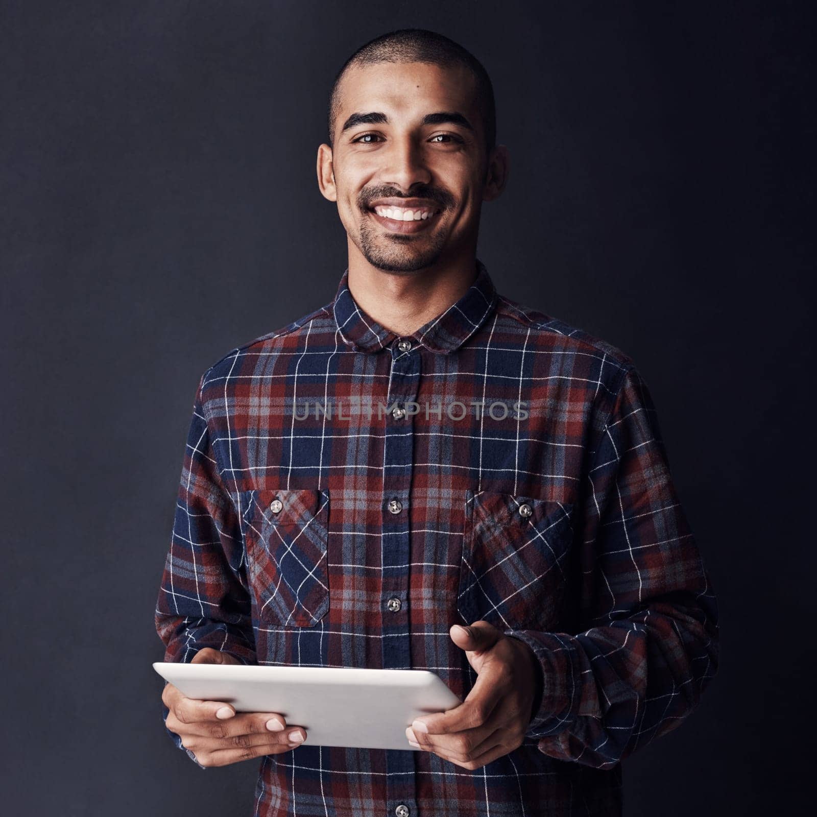 Cool, calm and connected. Studio portrait of a young man using a digital tablet against a dark background. by YuriArcurs