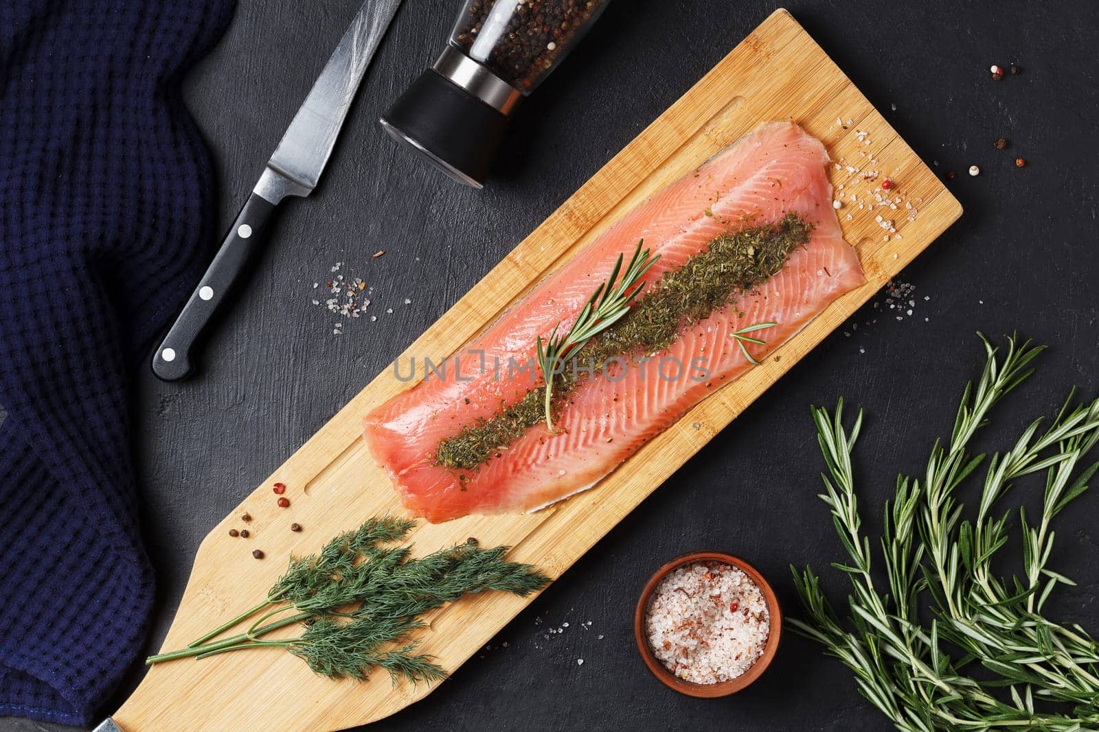 Salted fish fillet with spices and herbs:dill and rosemary on a wooden board on a black background. by lara29
